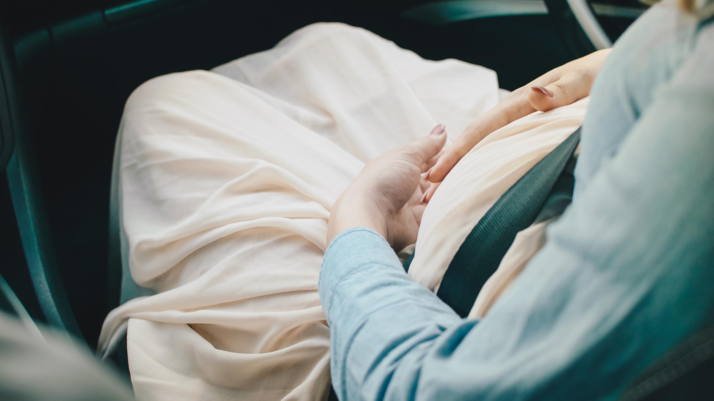 A pregnant woman sitting in the car with hands on her belly