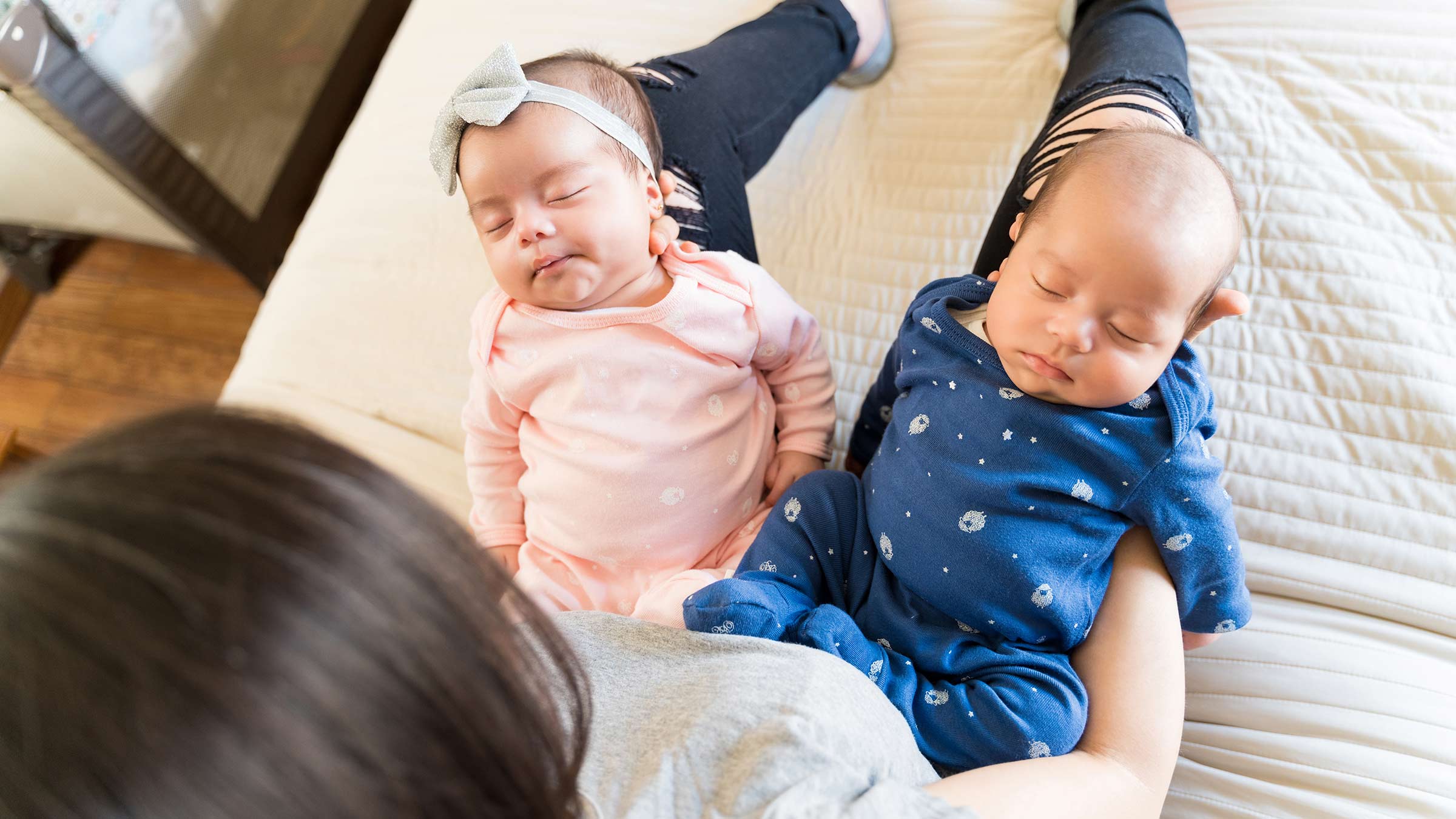 A mother holding twin babies on her bed