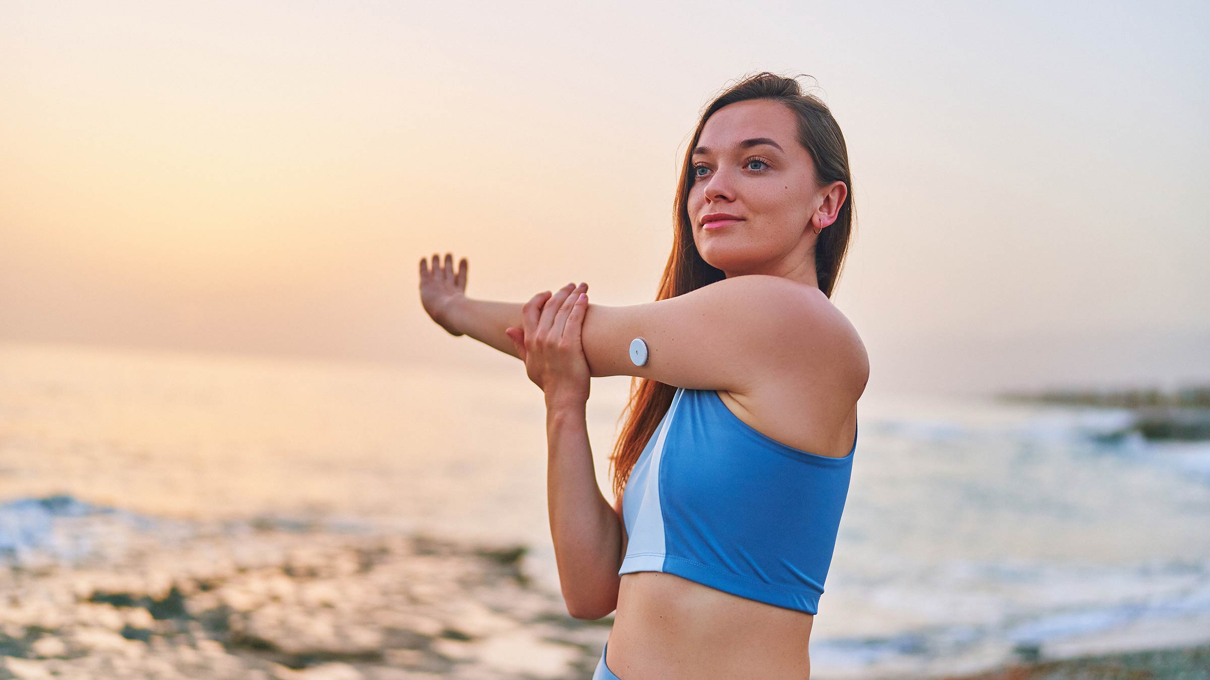 A slim woman with type 1 diabetes stretching by the ocean