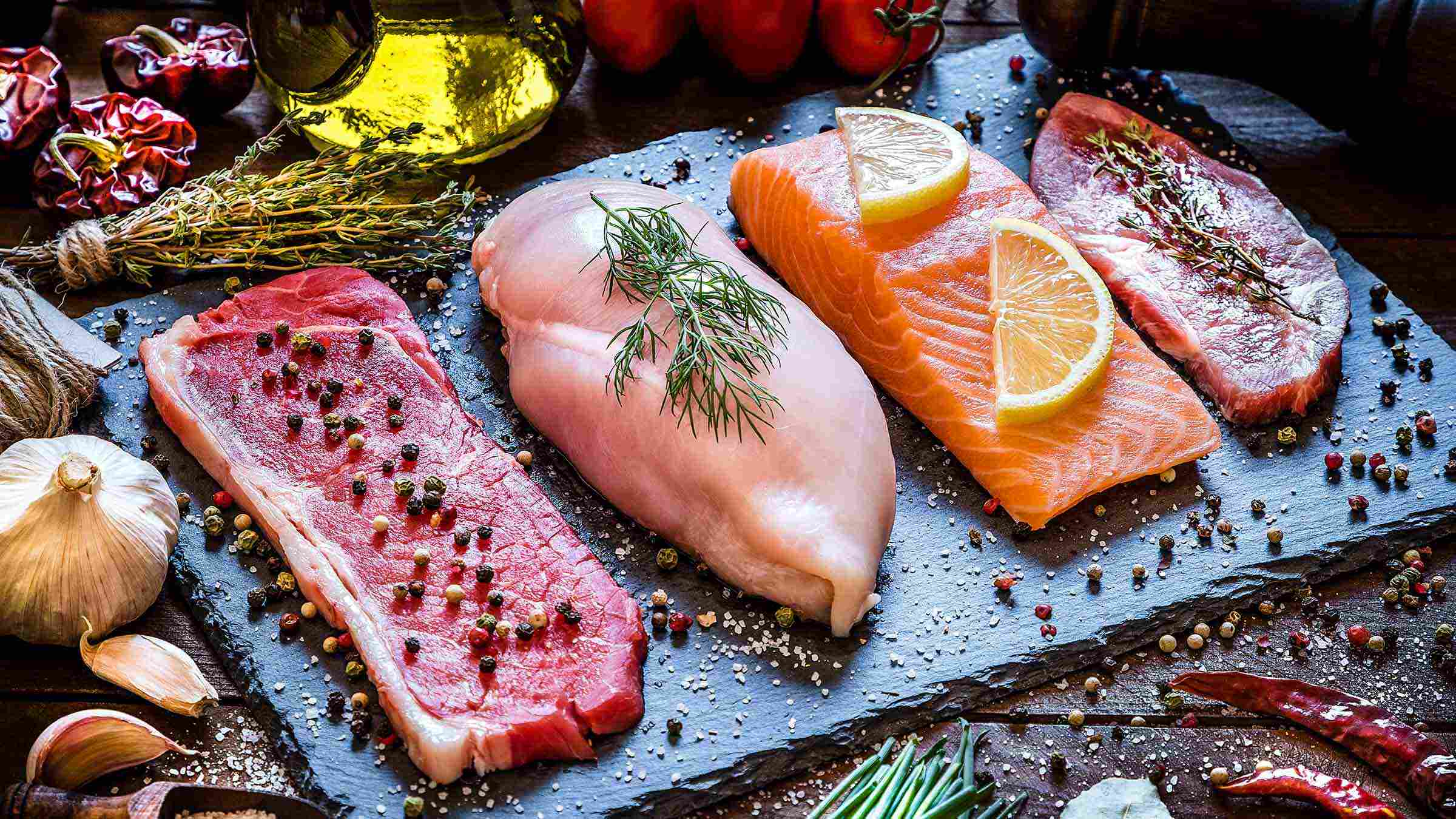 A beef steak, a chicken breast, a salmon fillet and a pork steak on a stone tray