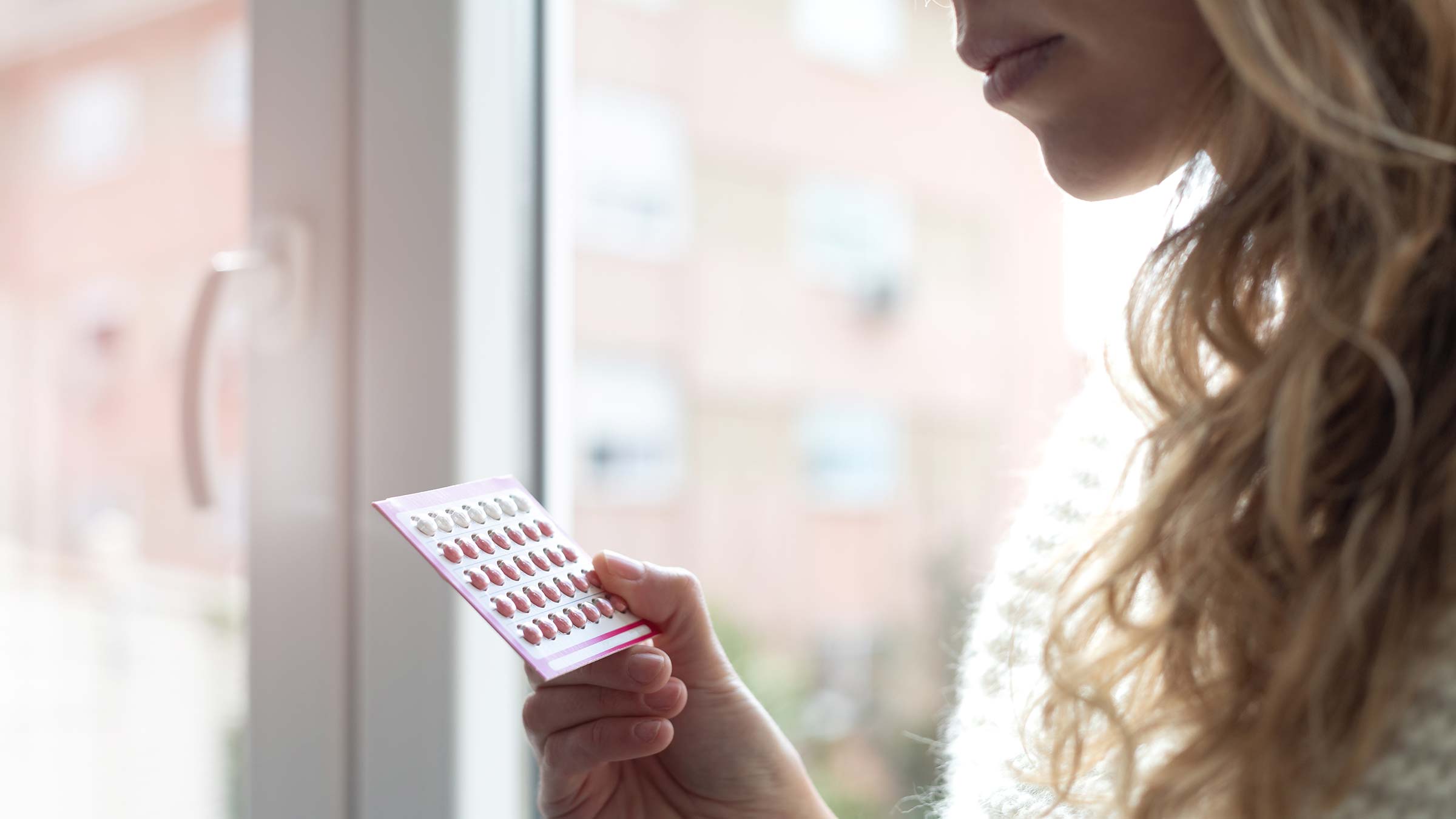 A young woman holding a package of birth control pills
