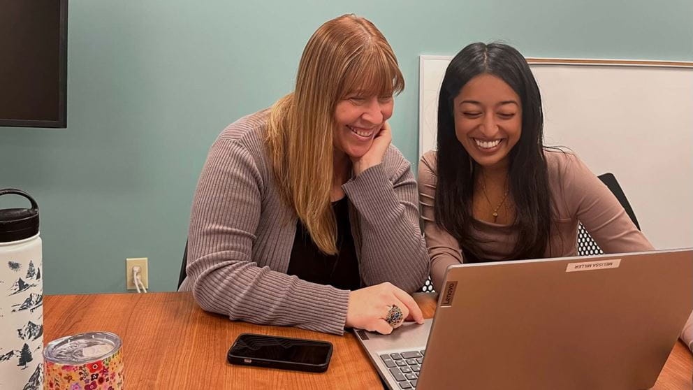 Melissa Miller and Noureen Bhuiya smiling while looking at a laptop computer