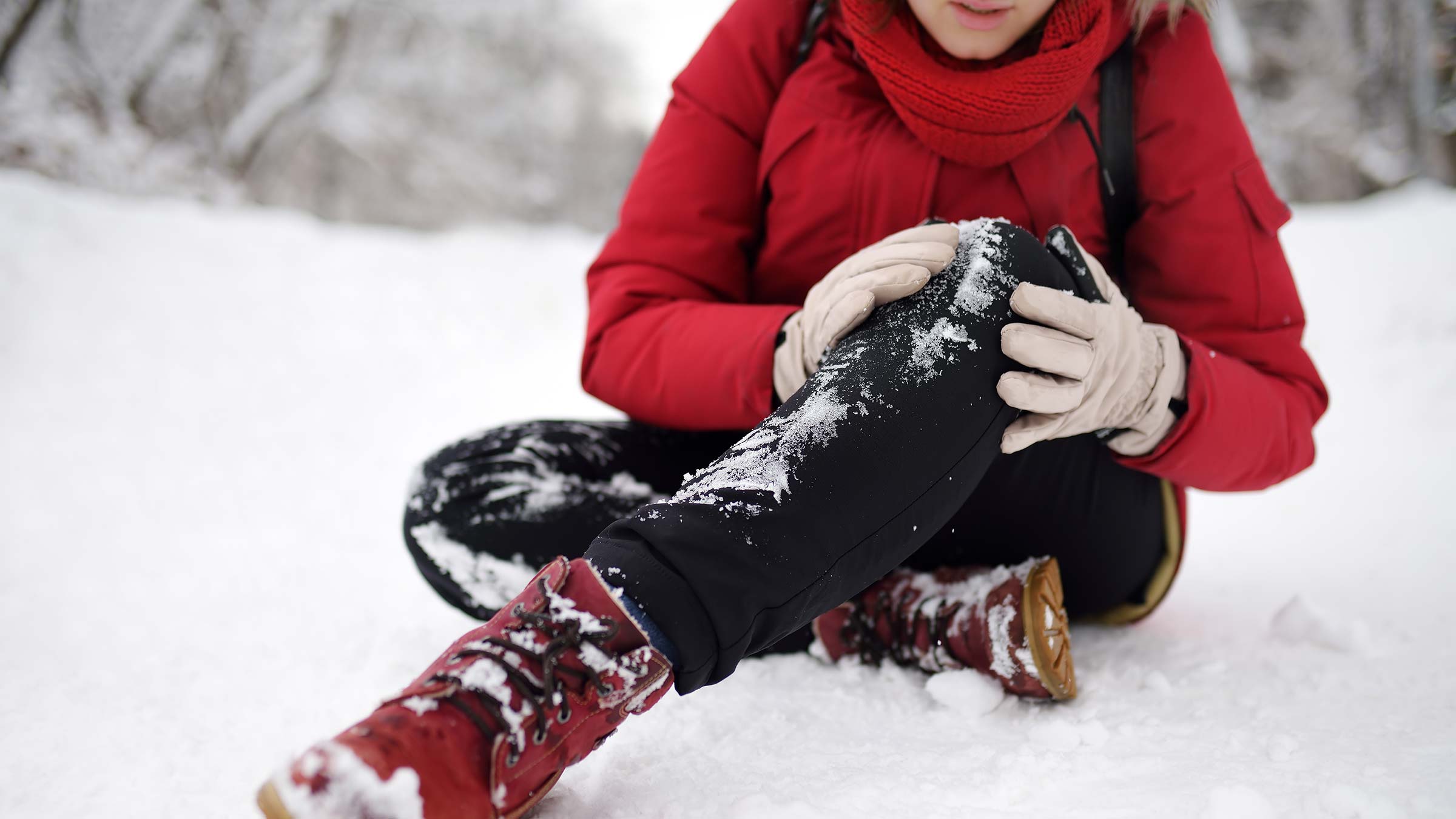 Woman sitting on a snow holding her knee