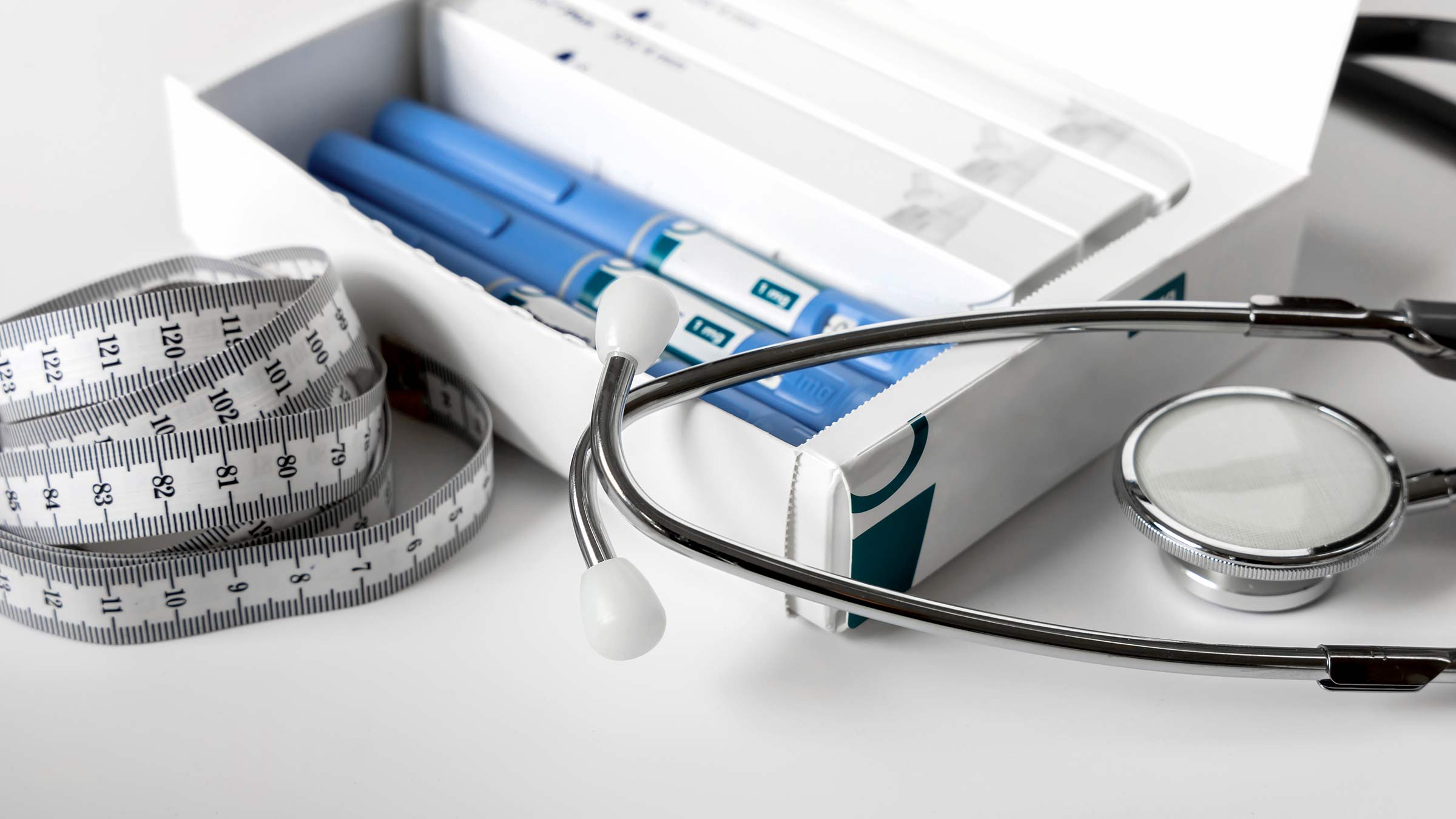 Measuring tape, stethoscope, and a box of weight loss injection pens sitting on a table