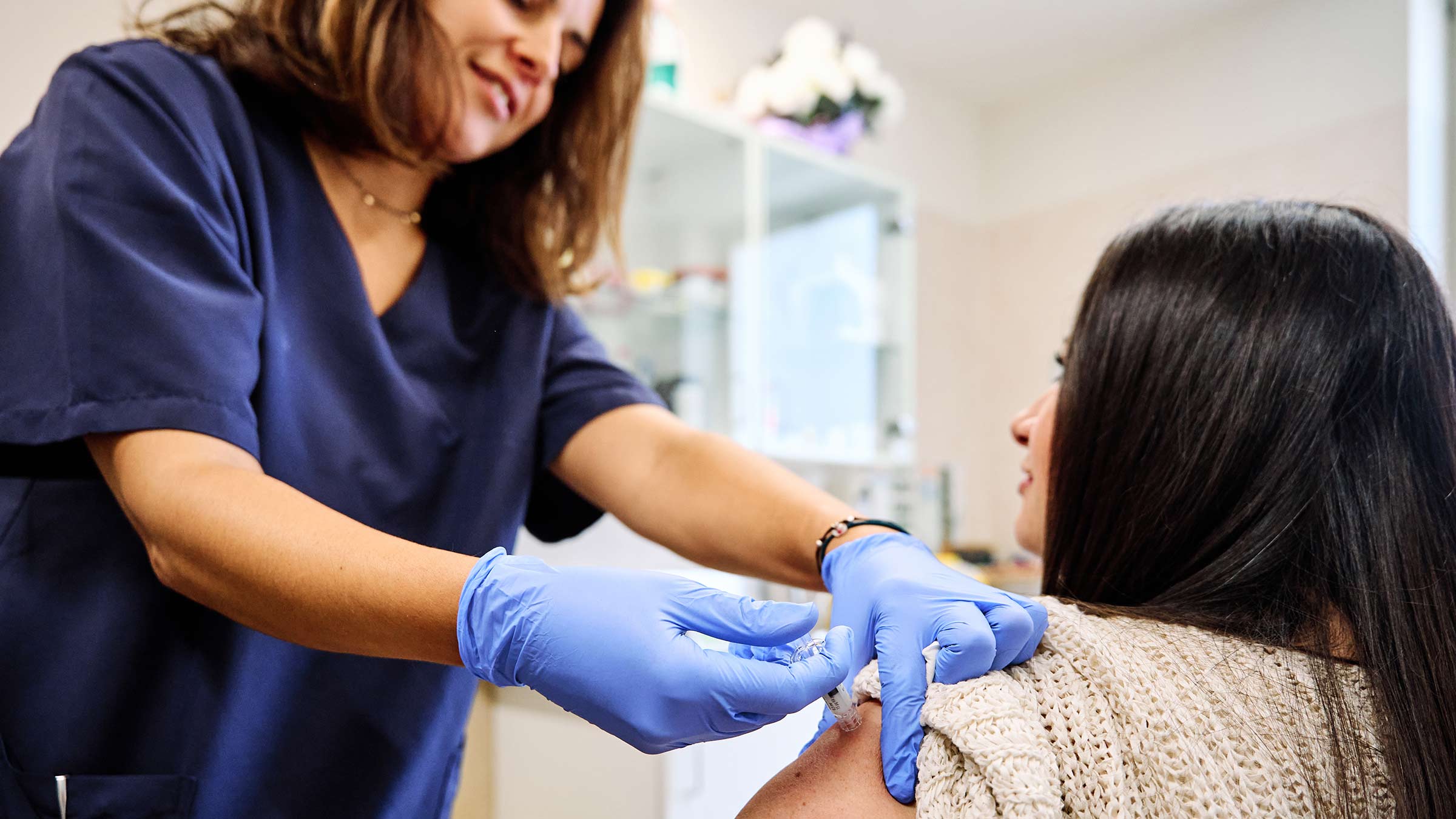 A woman receiving a shot in her arm from a female medical professional