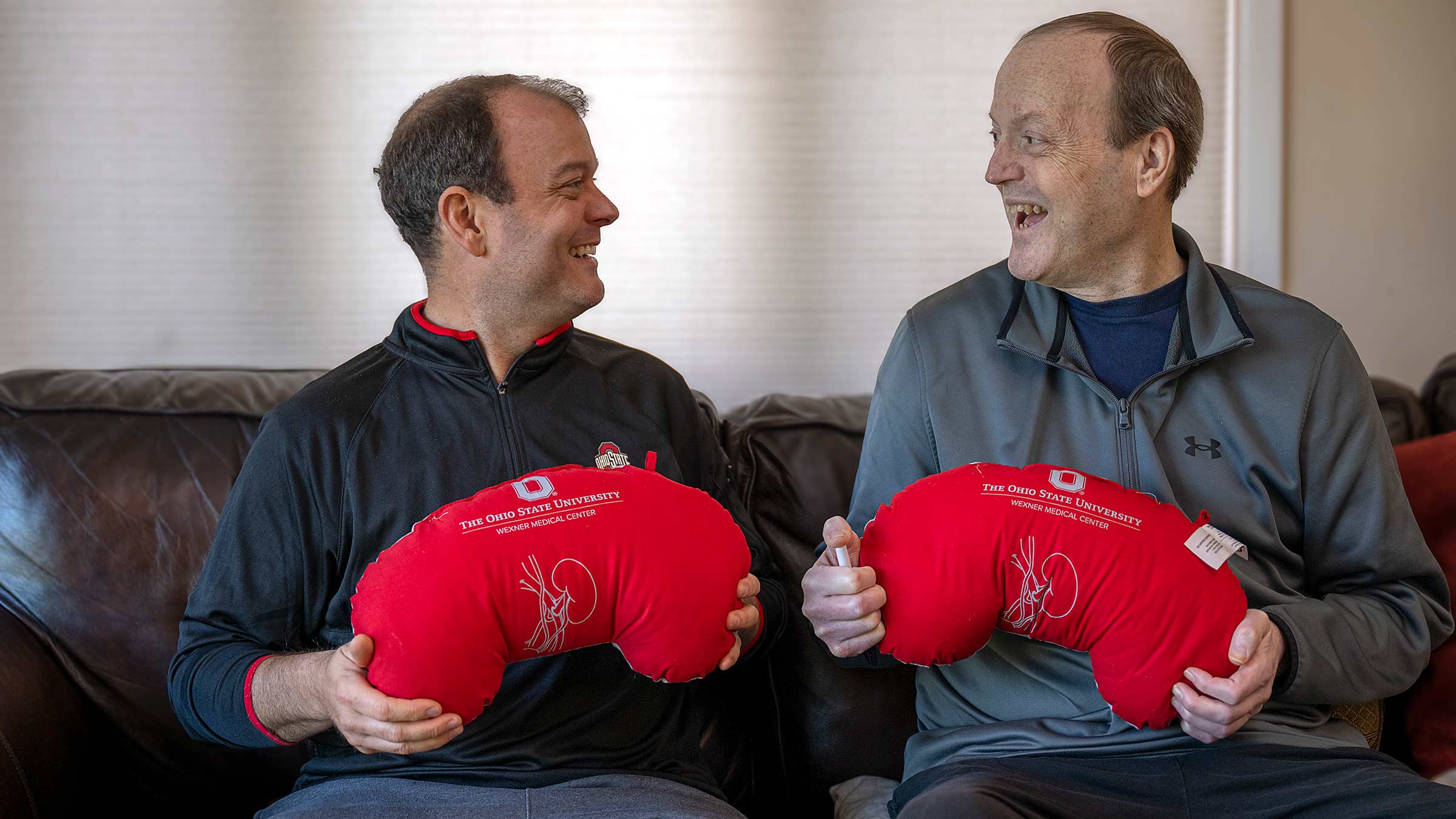 Steve and Mike Robinson looking at each other smiling while holding red kidney-shaped pillows