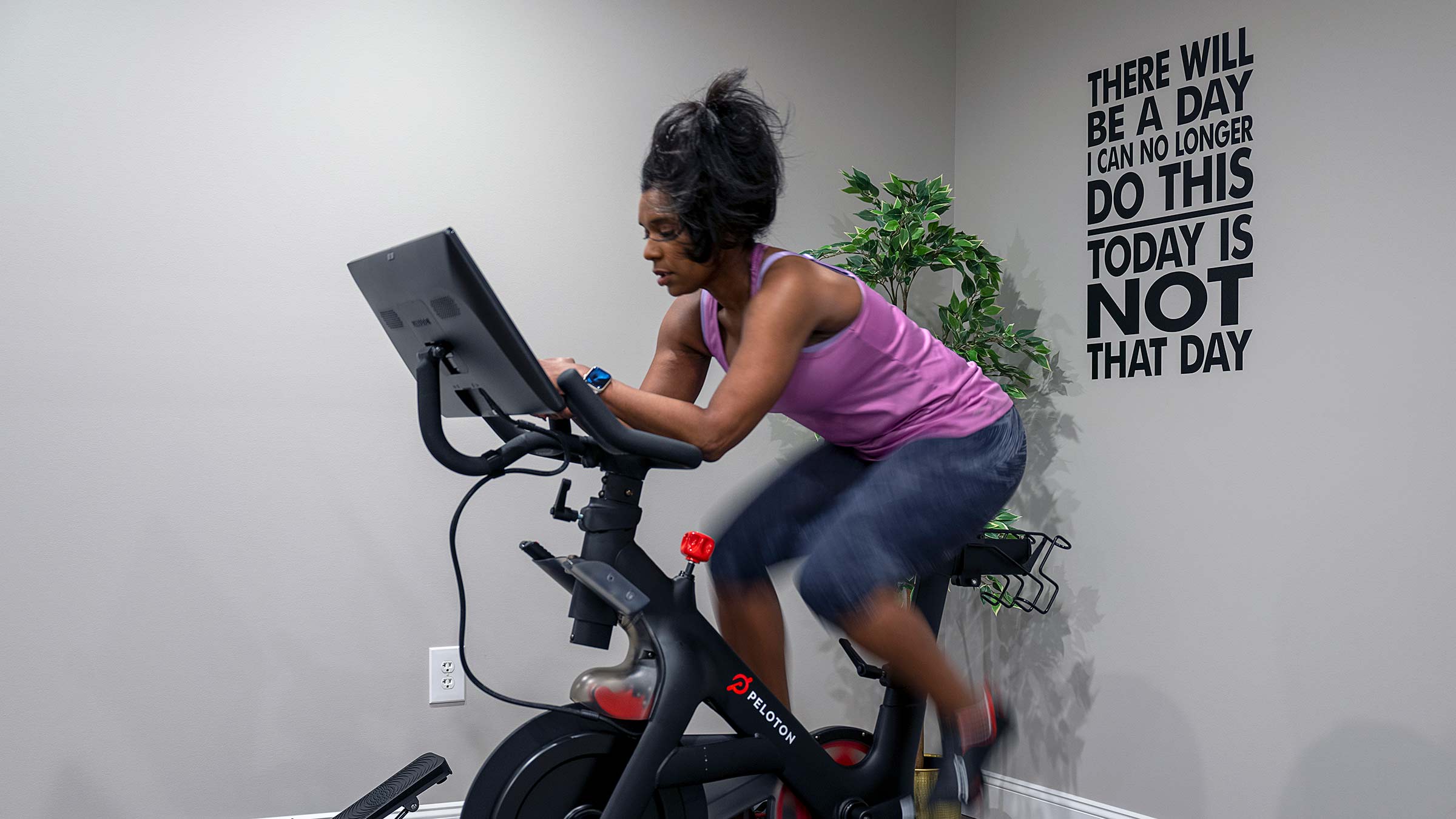 Paula Cole working out on a Peloton with the words on the wall behind her: "There will be a day I can no longer do this, today is not that day."
