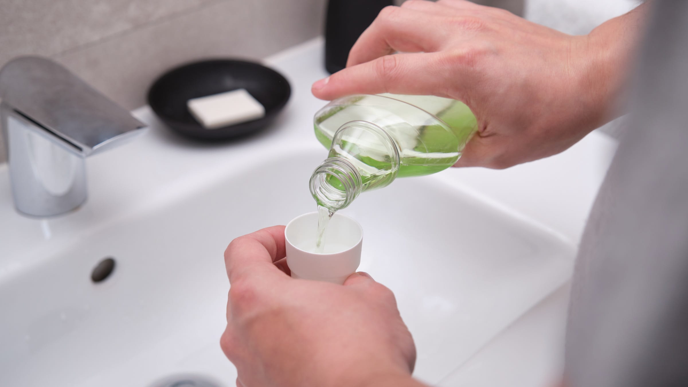 Man pouring mouthwash from a bottle into a cap in the bathroom