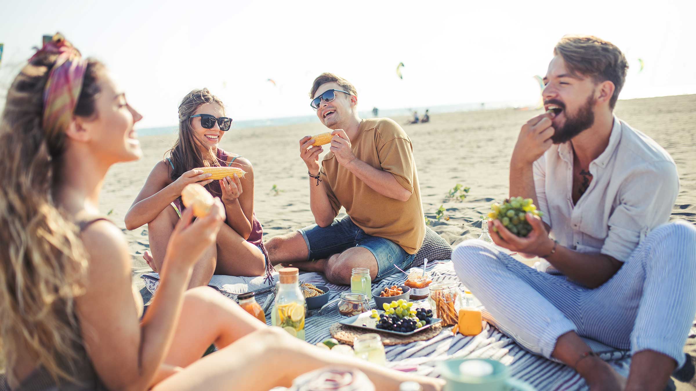 Friends eating corn on the cob and grapes on the beach