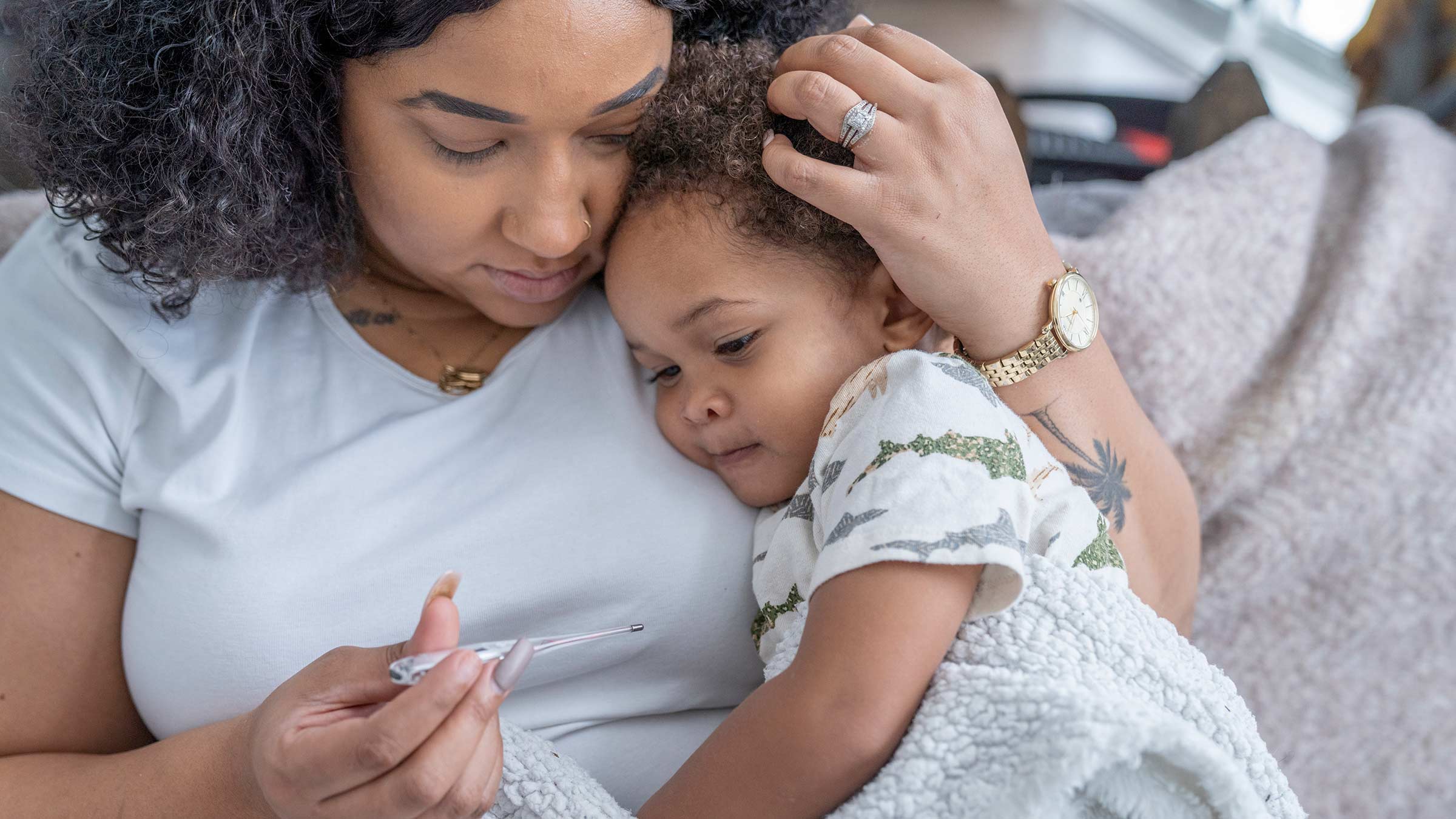 Mother holding her sick child with a thermometer in her hand