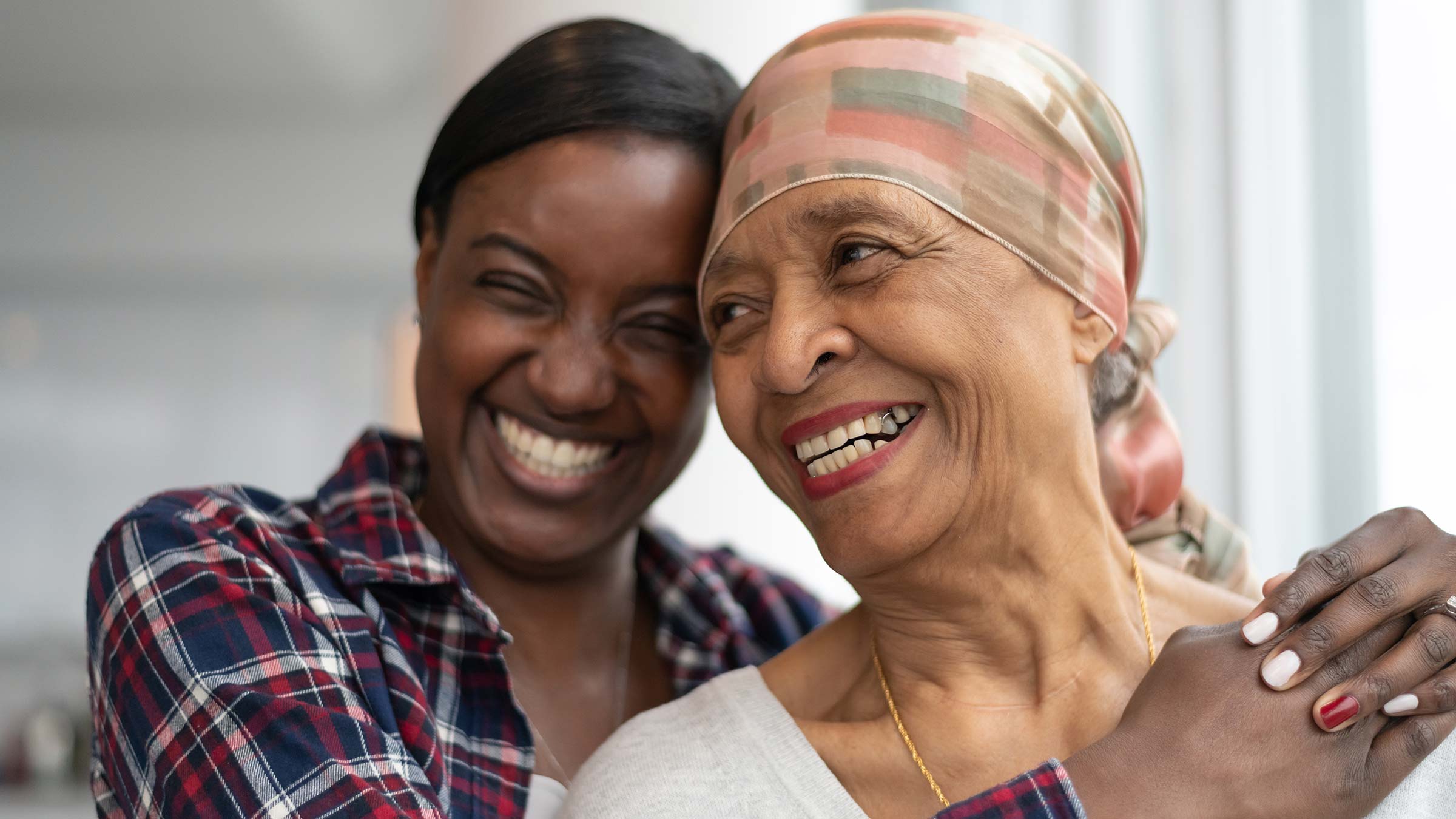 A senior African American woman with cancer is hugged by her adult daughter