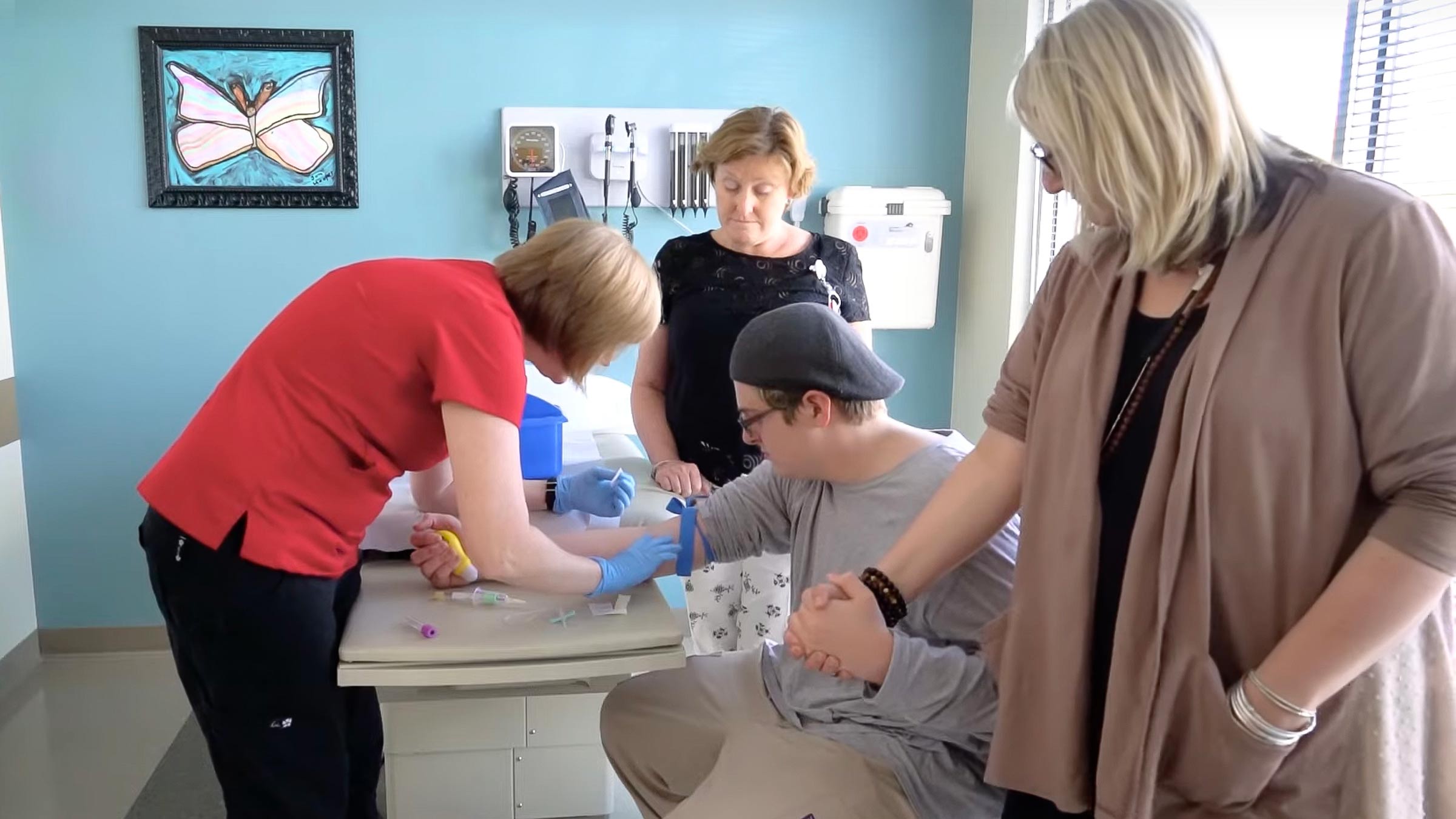 A woman holding an autistic patient's hand, while a nurse prepares to draw blood