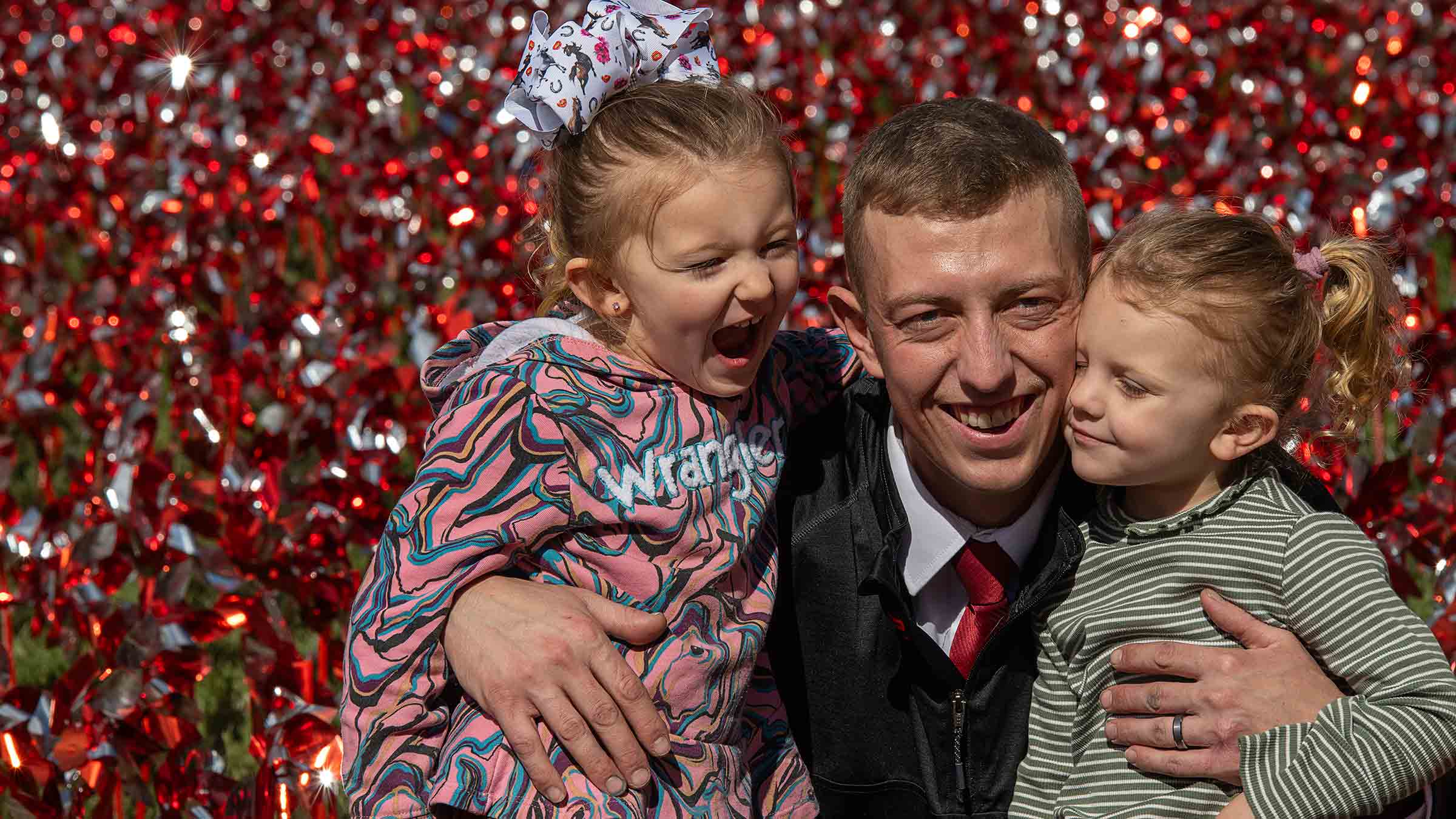 Justin Shupert hugging his two daughters with pinwheels on the background