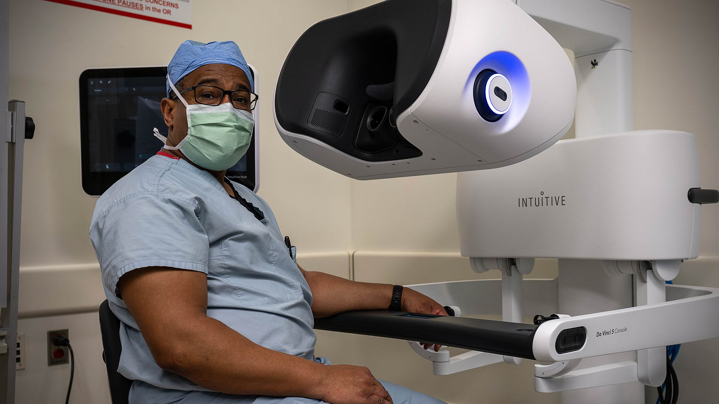 Dr. Robert Merritt in surgical scrubs looking up from the da Vinci 5 surgical robot