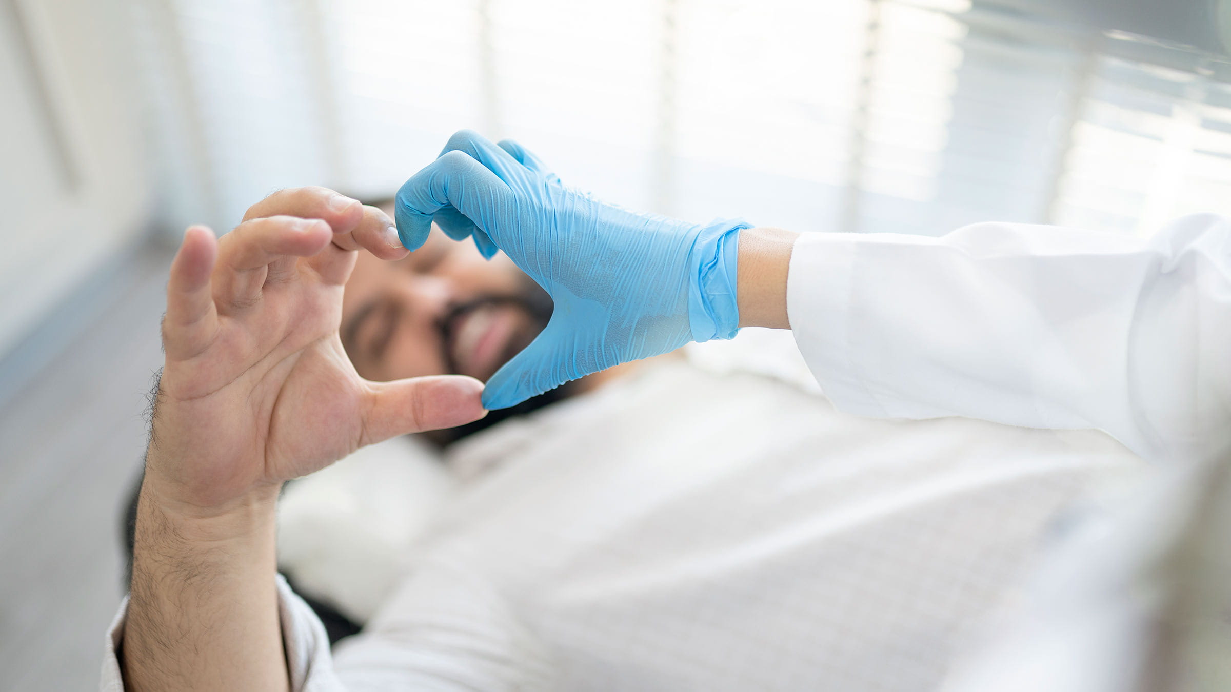 A patient in a hospital bed makes half of a heart shape with their hand, while a sterile-gloved hand makes the other half