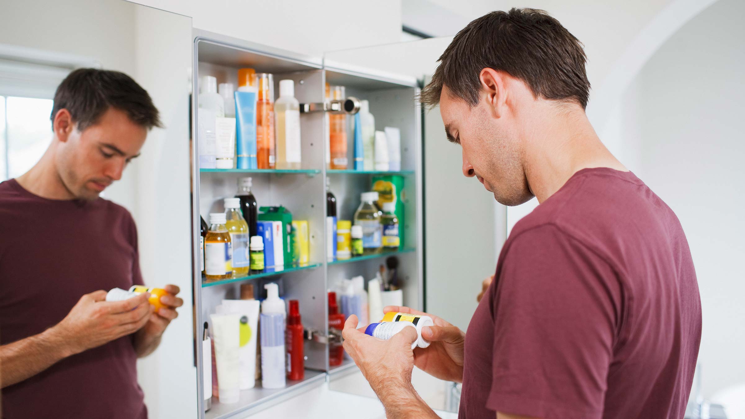 Man reading bottle labels while standing in front of an open medicine cabinet