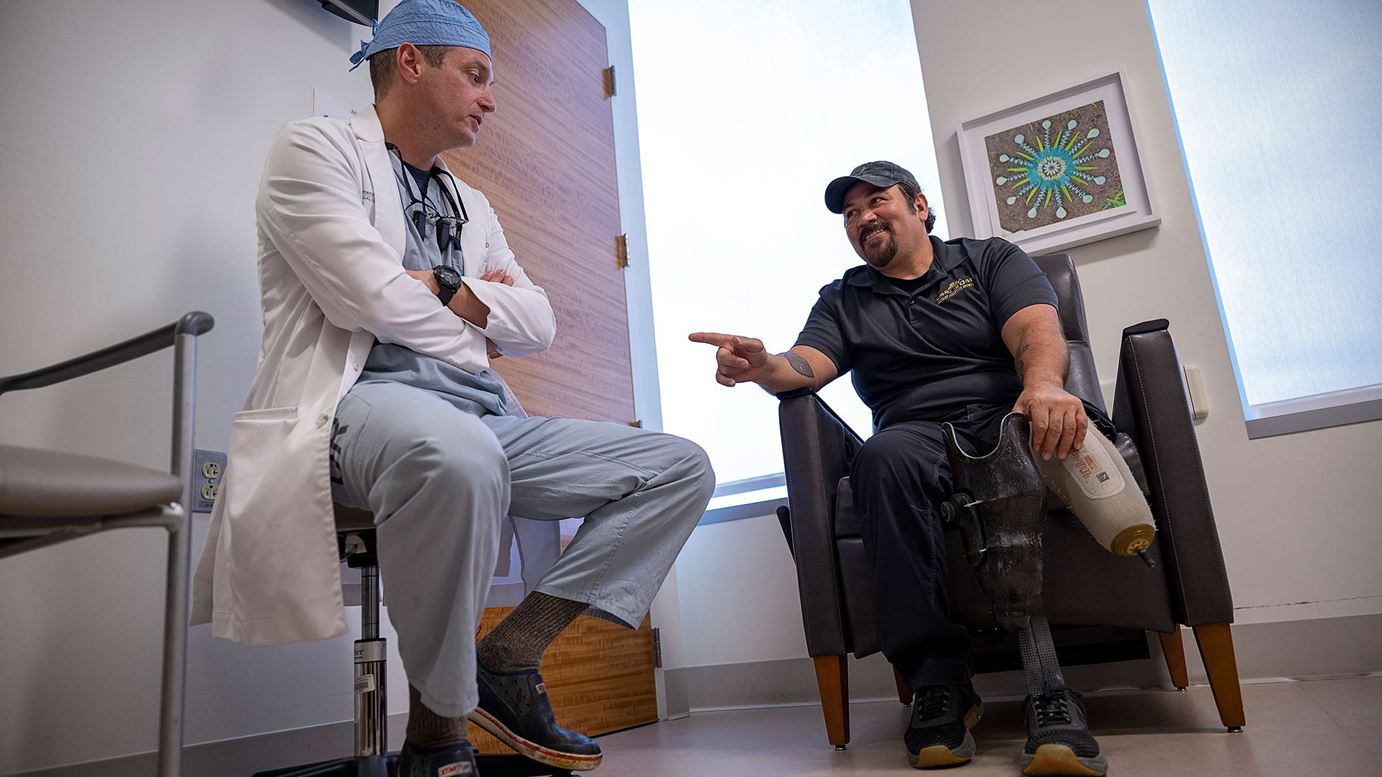 Jason Souza, MD, listening to a patient who is holding his prosthetic leg 