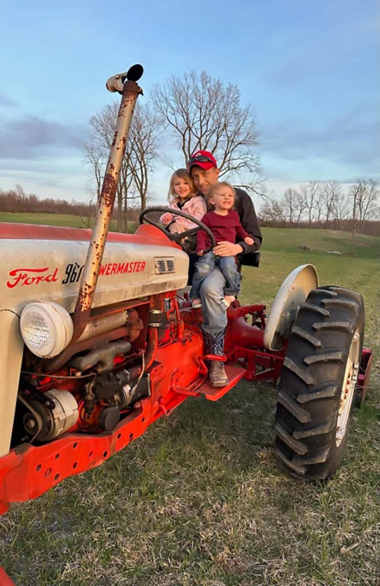 Justin Shupert sitting on a tractor holding his children