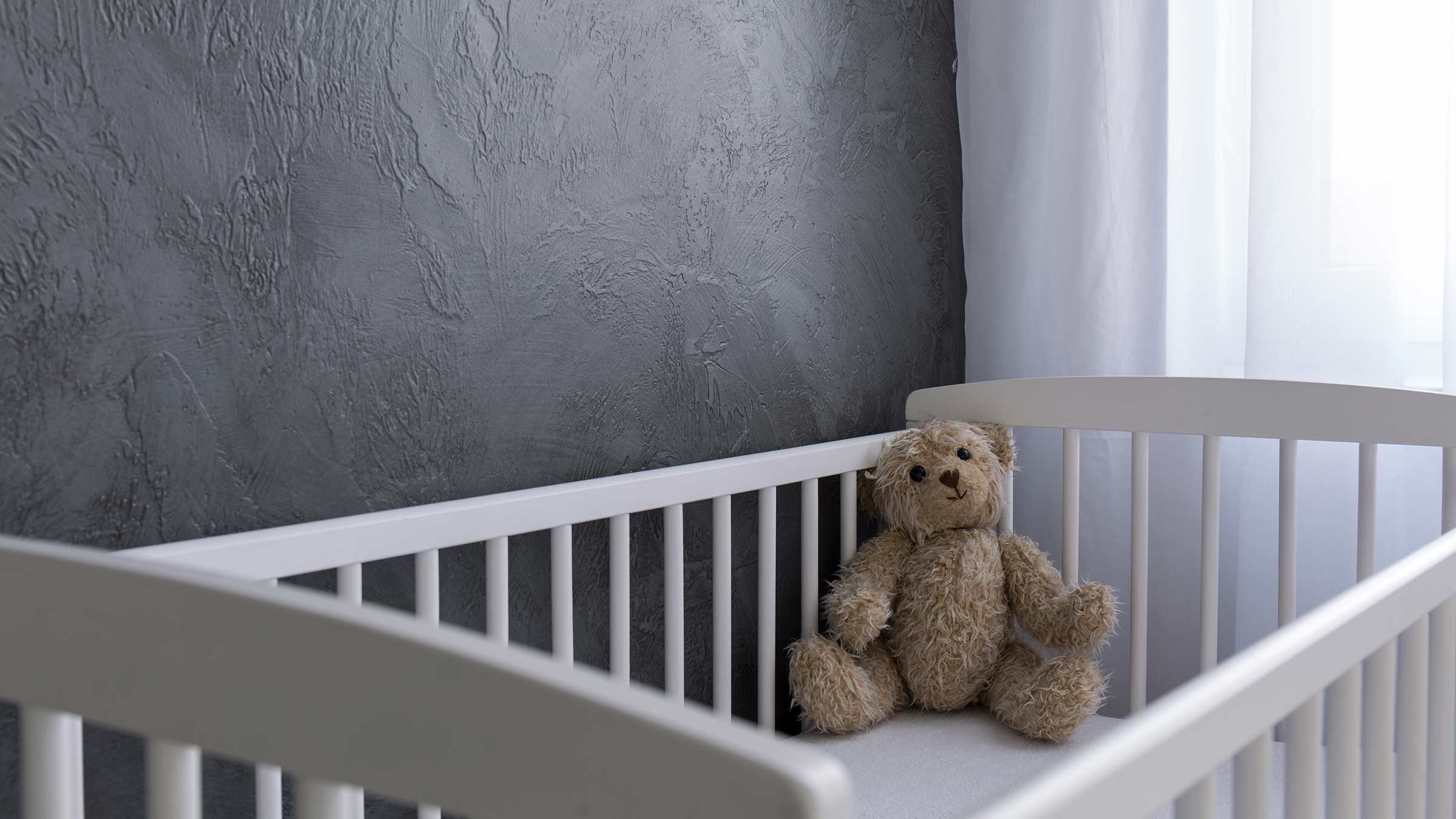 Baby crib with a teddy bear against a gray painted wall