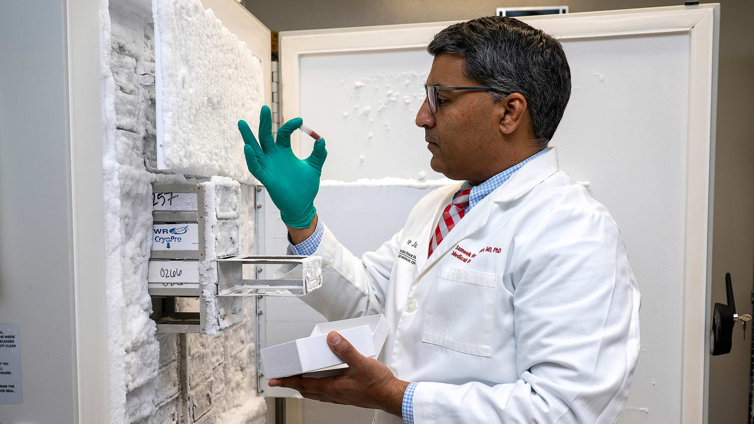 Sameek Roychowdhury, MD, PhD, holds a sample tube next to a genetics freezer