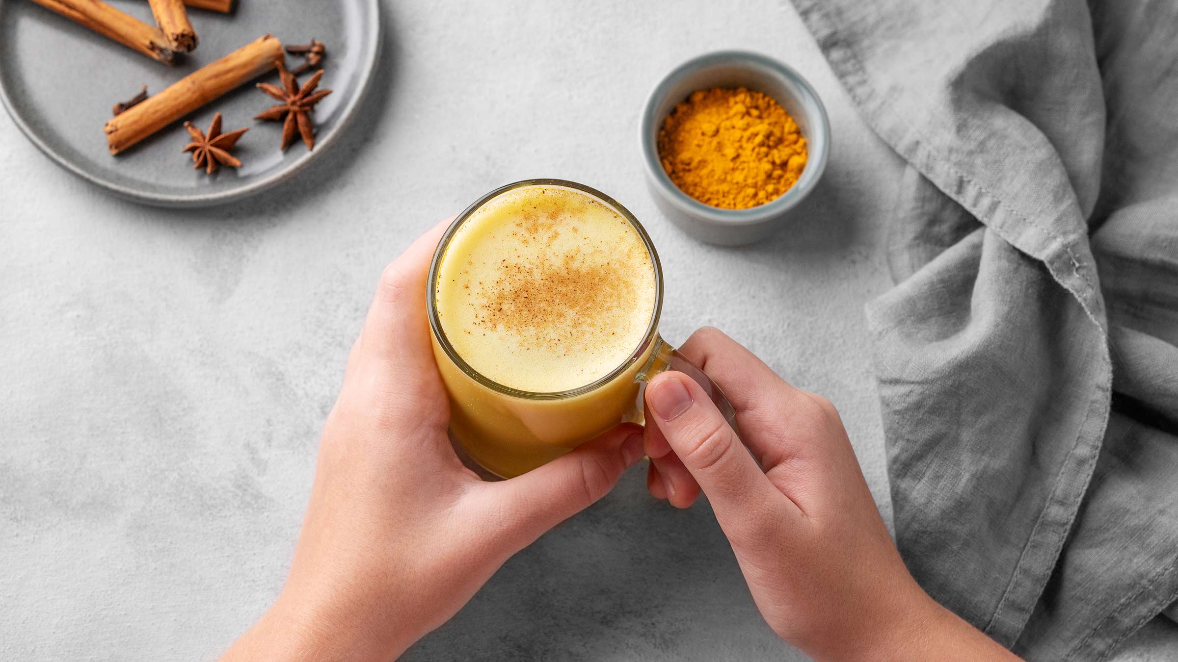 Hands holding turmeric golden milk latte with spices