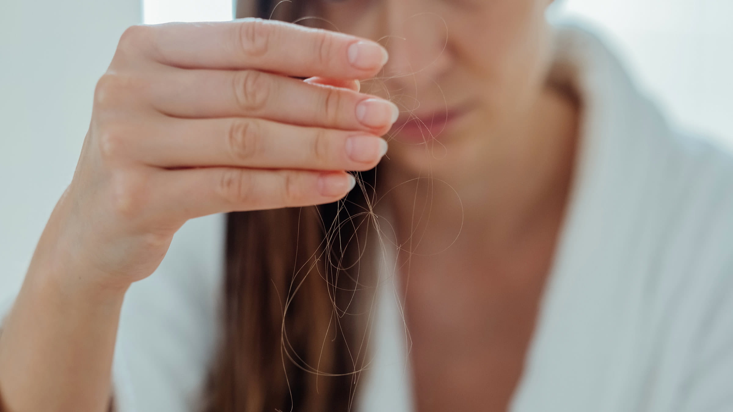    A young woman holding strands of fallen out hair between her fingers