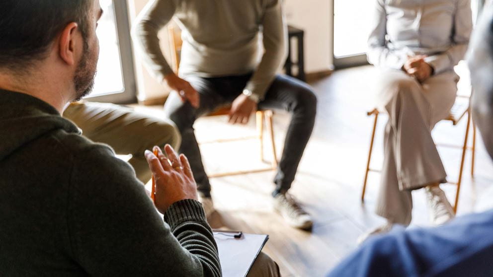 Male therapist guiding a group session with others sitting in a circle