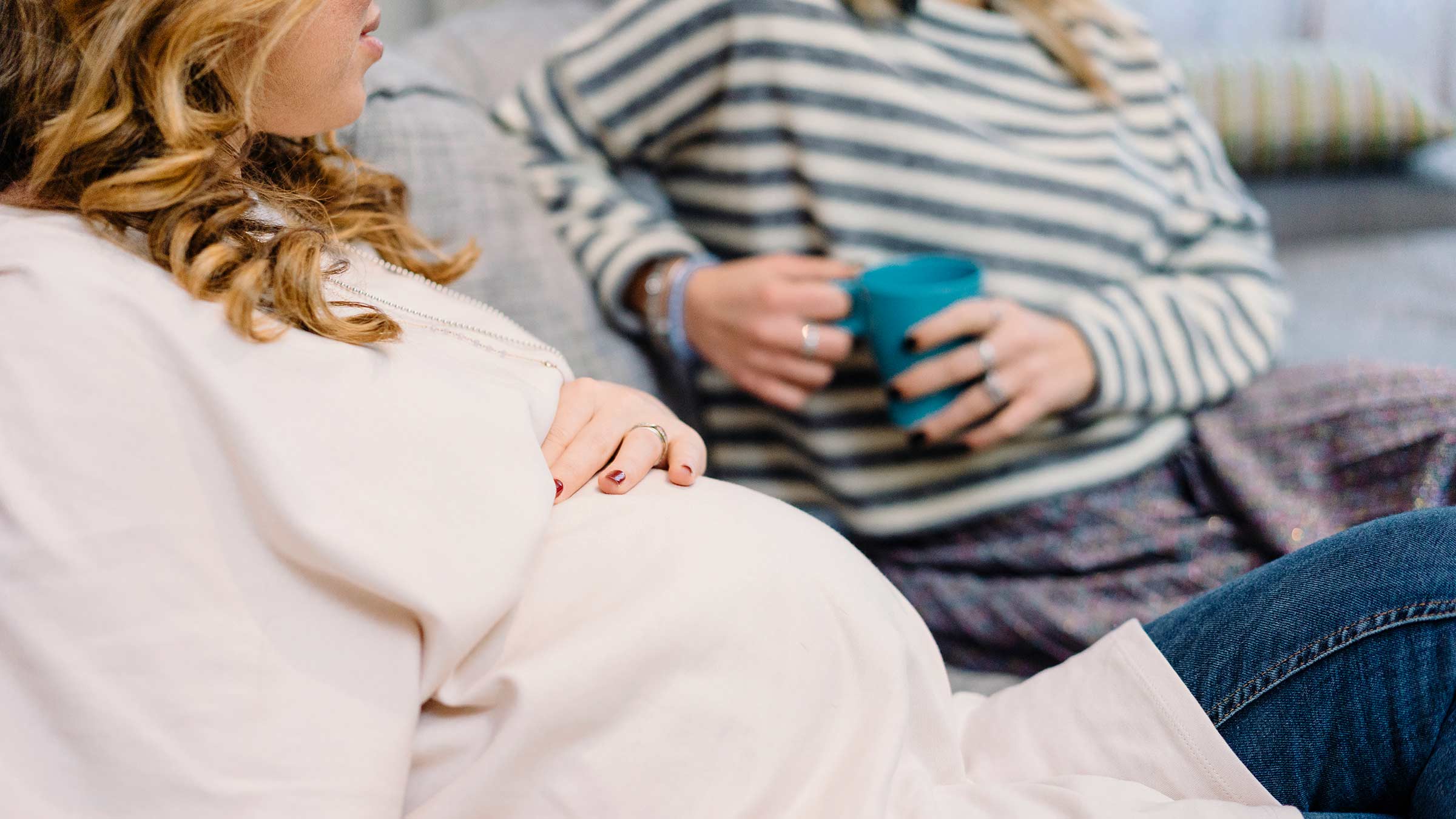 Pregnant woman and a friend have a conversation while sitting on a couch