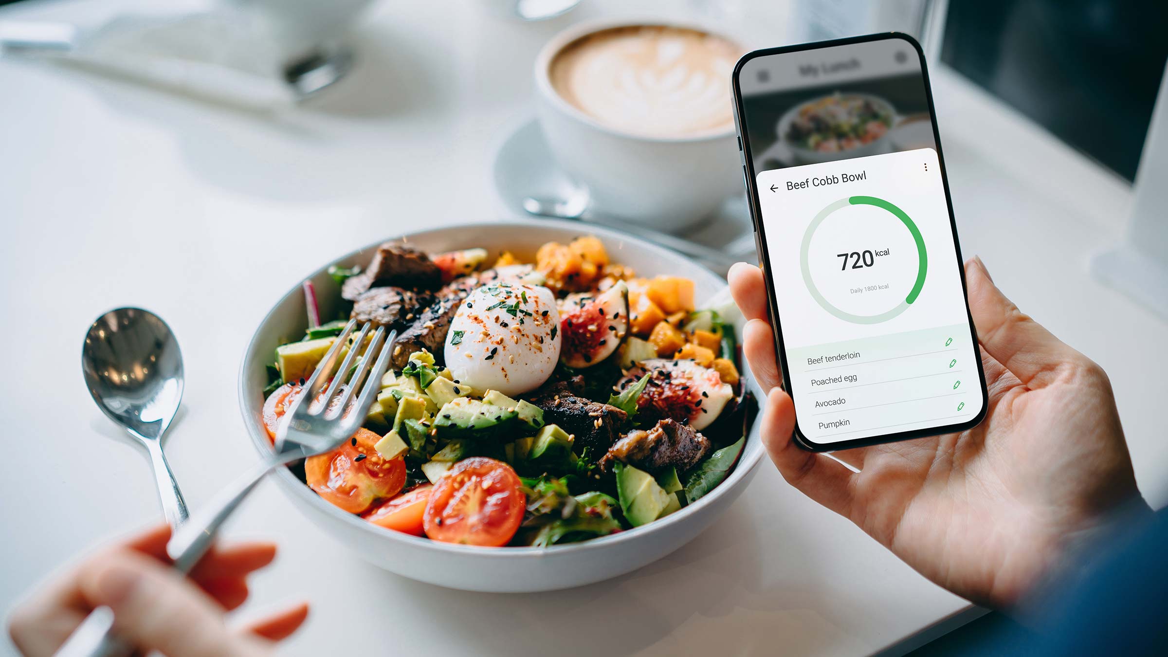 An individual sitting at a table with a salad while using a mobile phone to use a health app