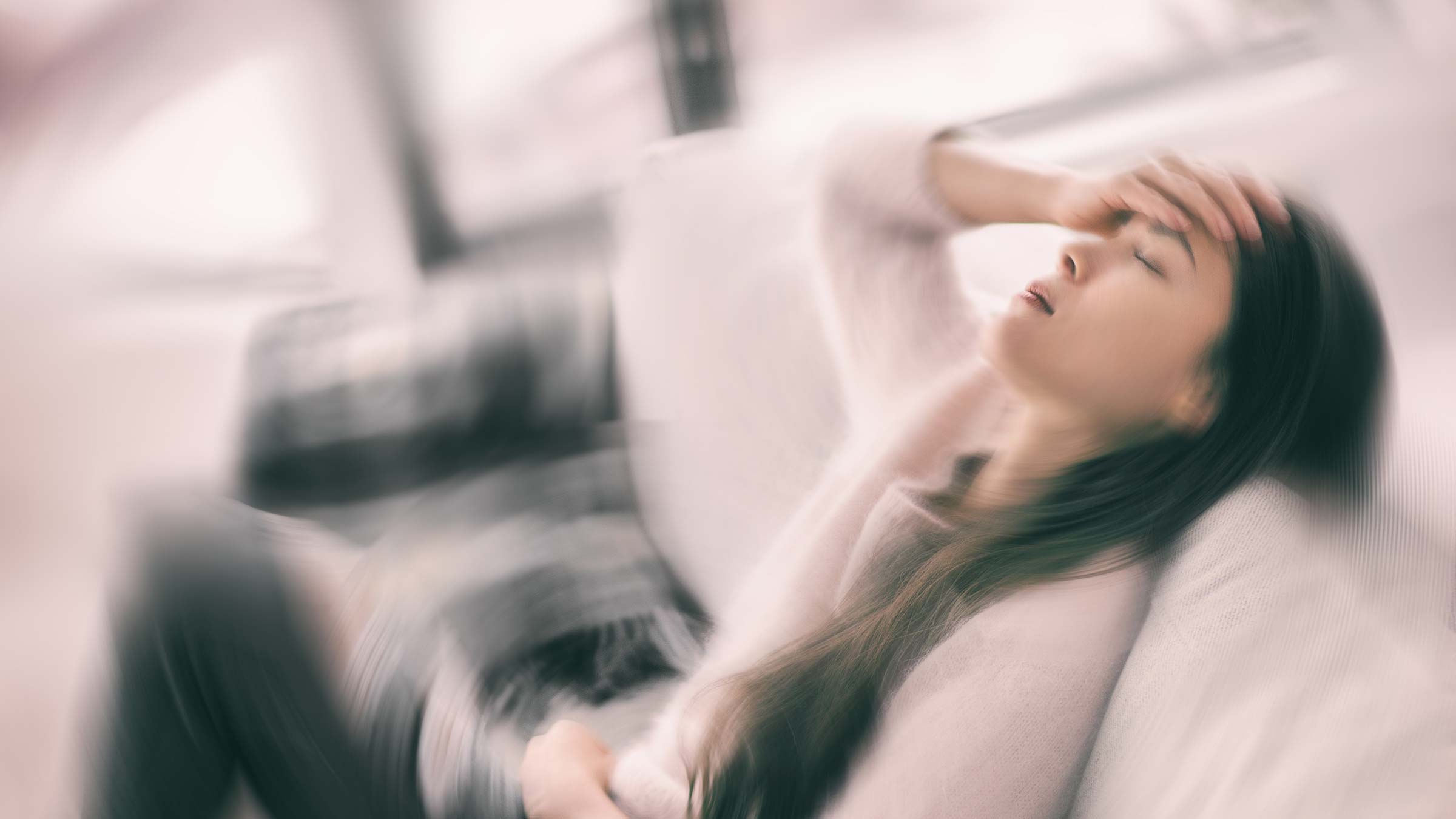 Blurry motion image of a woman holding her head and falling onto a couch