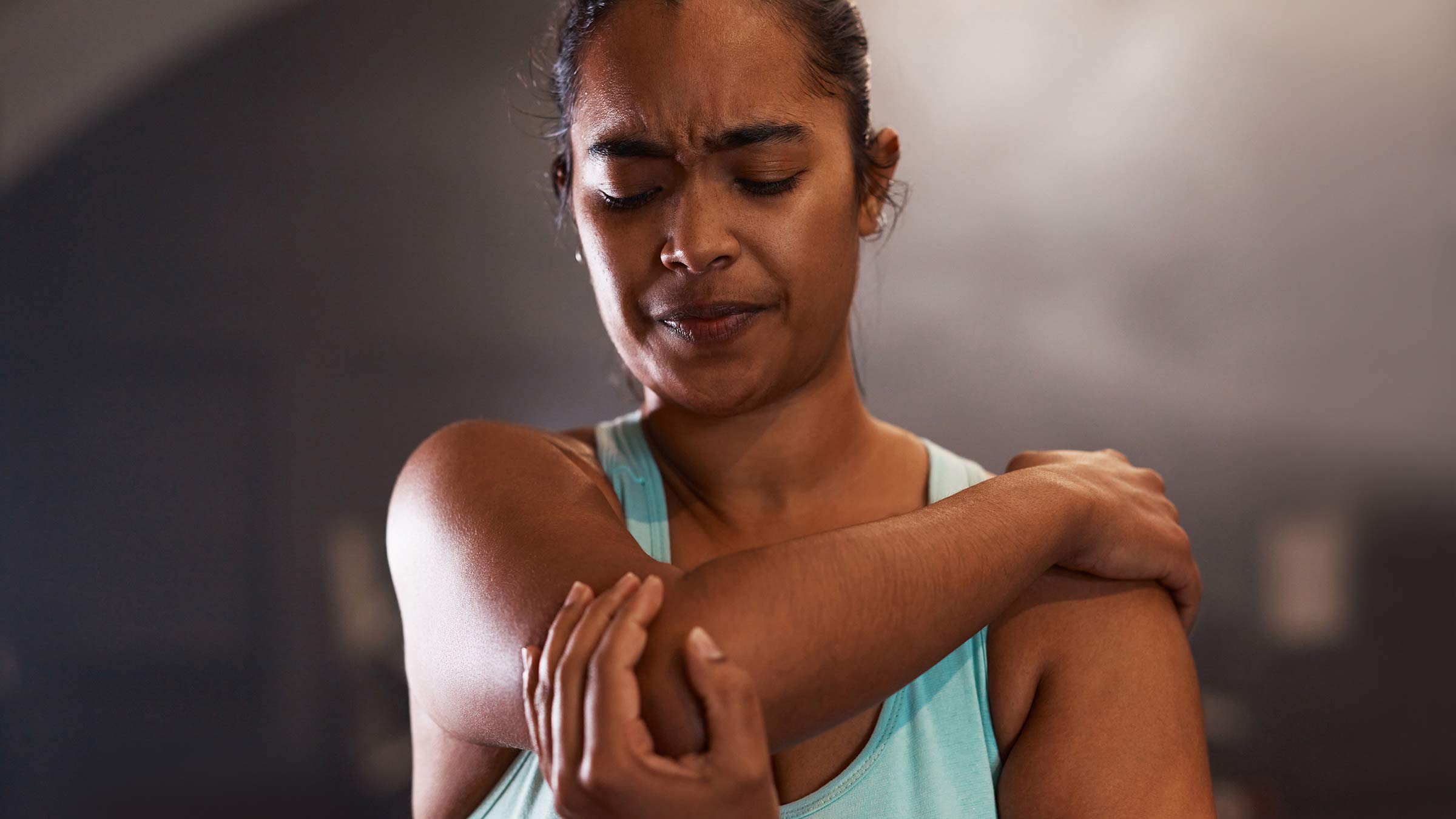 Young woman in athletic gear holding her elbow while experiencing pain