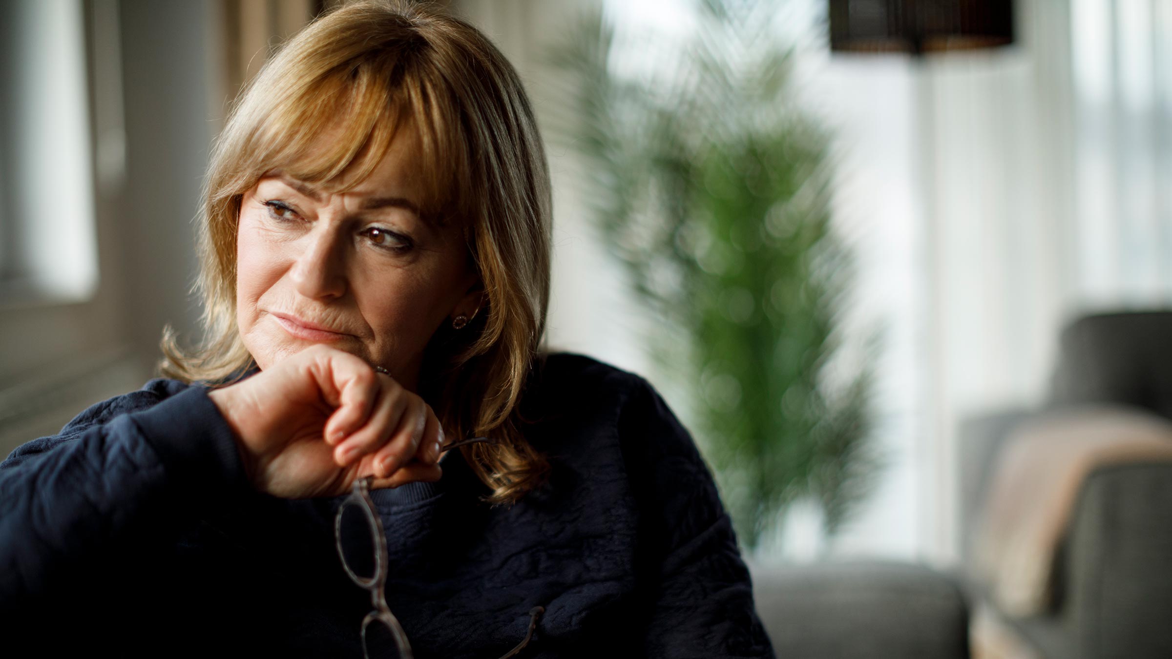 A menopause-aged woman sitting on a sofa and thinking