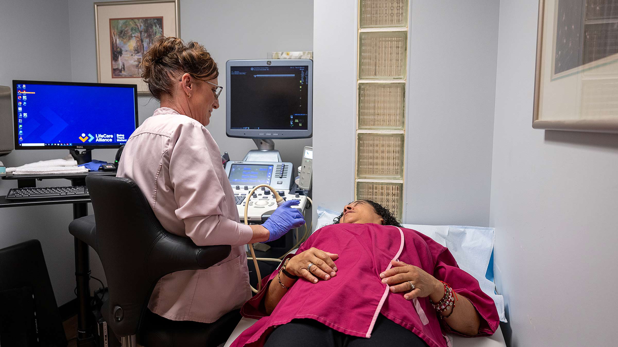 A woman lying down while a technician performing an ultrasound exam