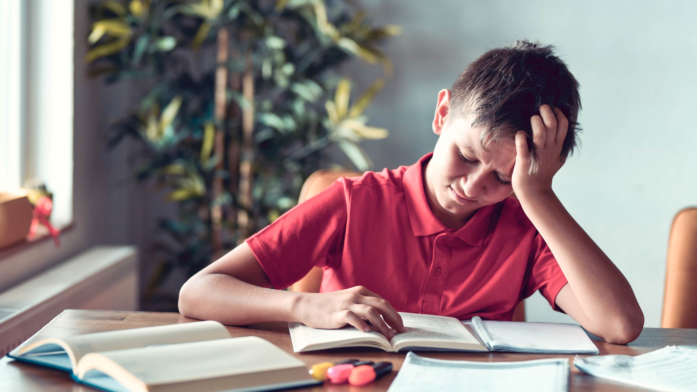 Young boy sitting at a table trying to read while dealing with a headache