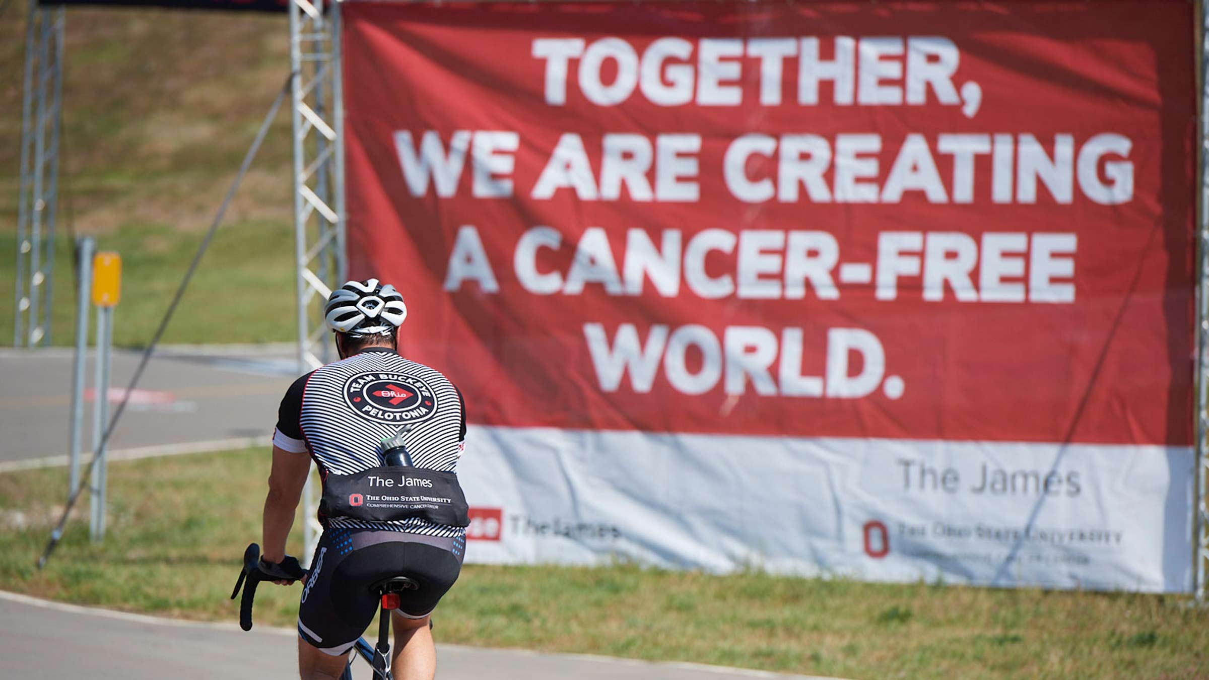 The rider biking past the banner: "Together, we are creating a cancer-free world".