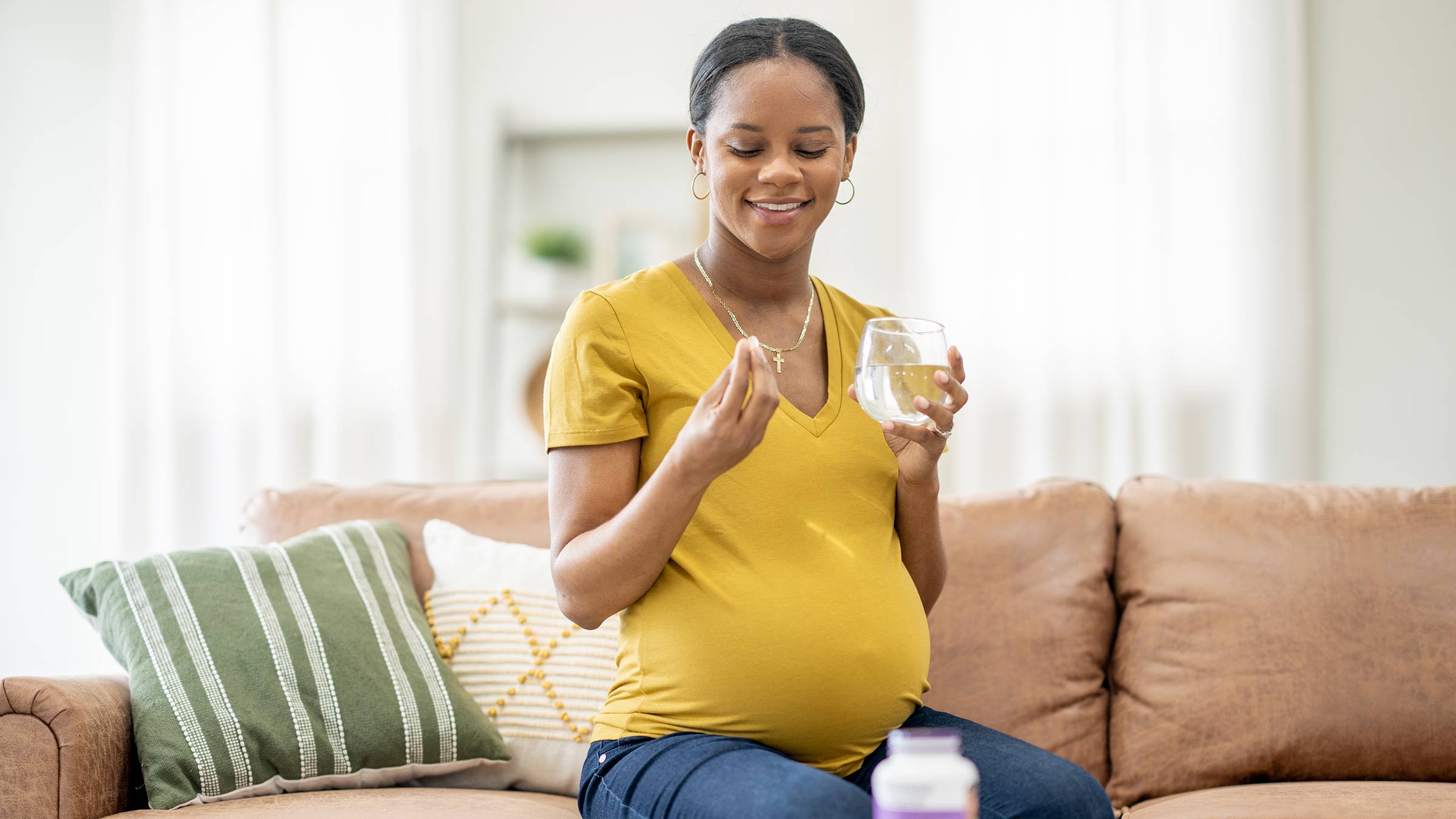 A young, pregnant woman taking a supplement with a glass of water