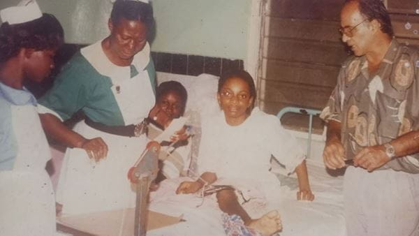 A young Joyce Amofah in a hospital bed being cared for by nurses