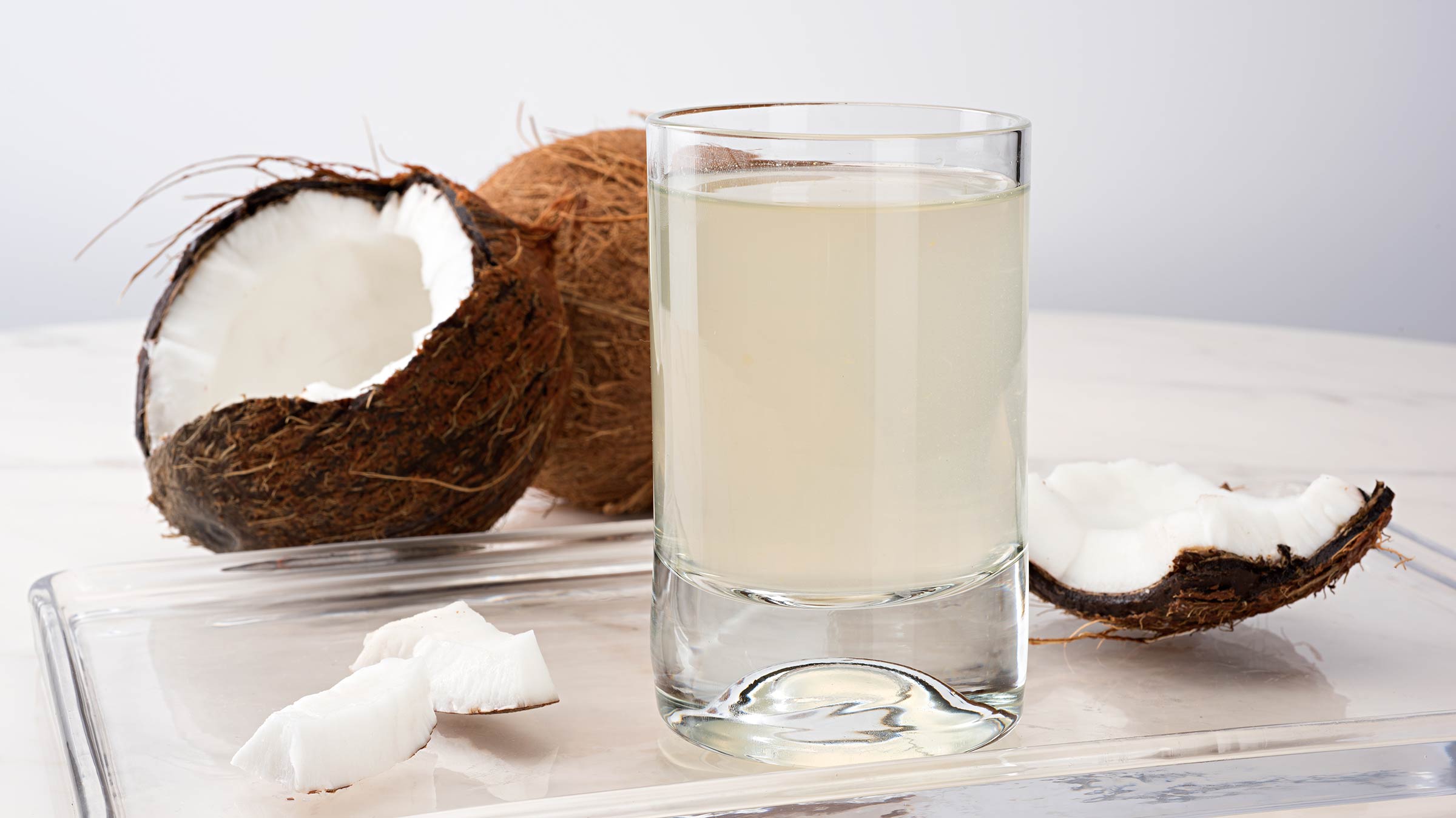 A glass of coconut water with a coconut on the background