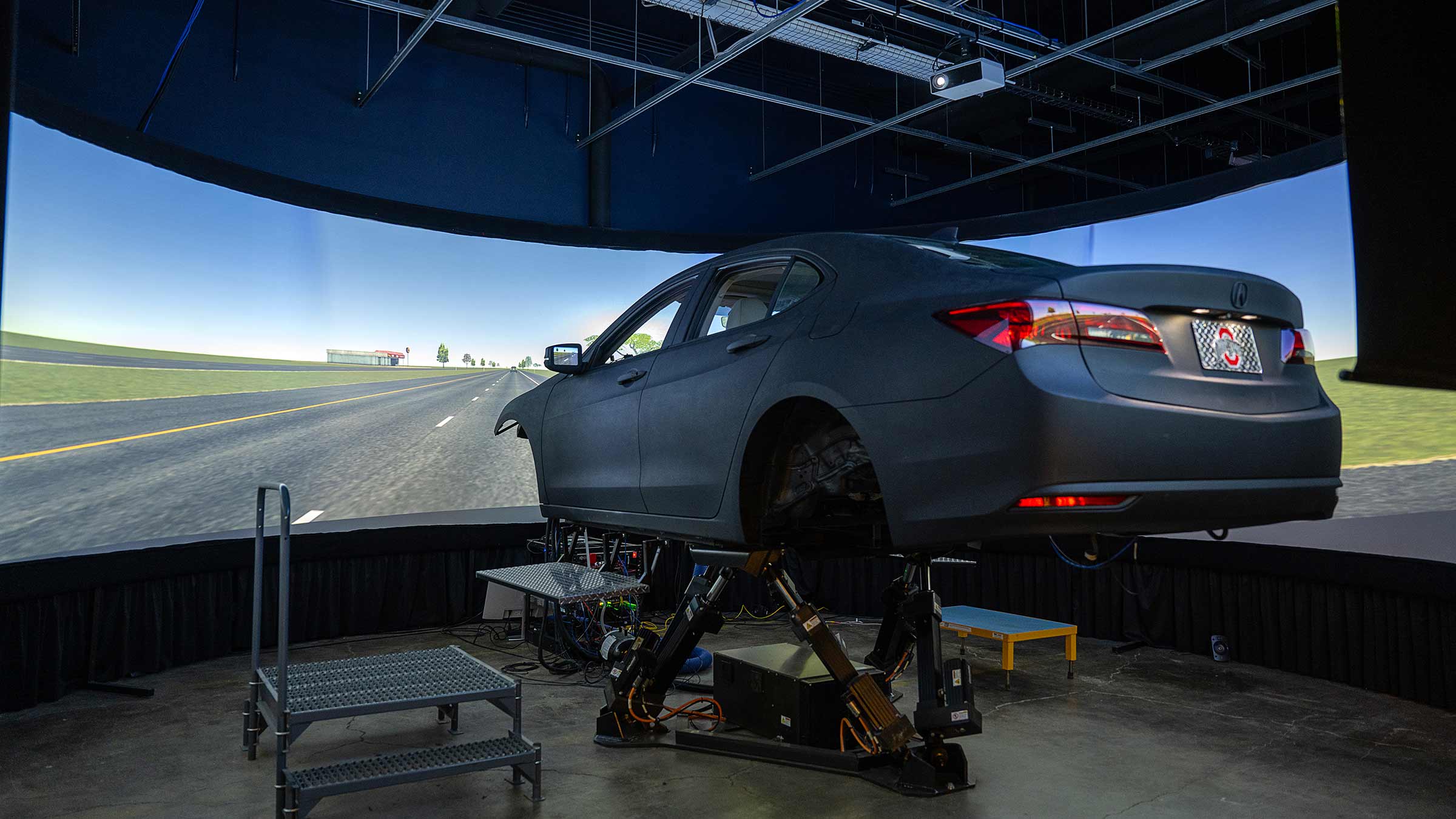 A driving simulator room with a screen and a car model in the center