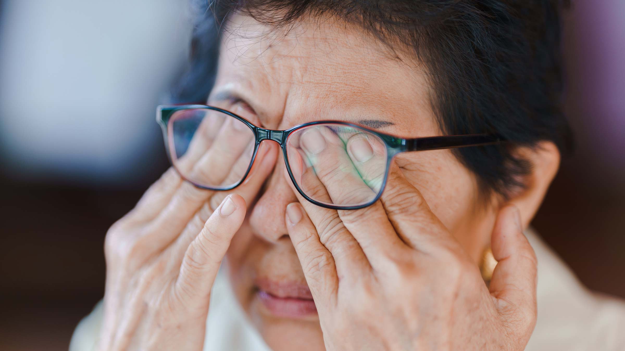 Elderly woman wearing glasses and massaging her eyes with her hands