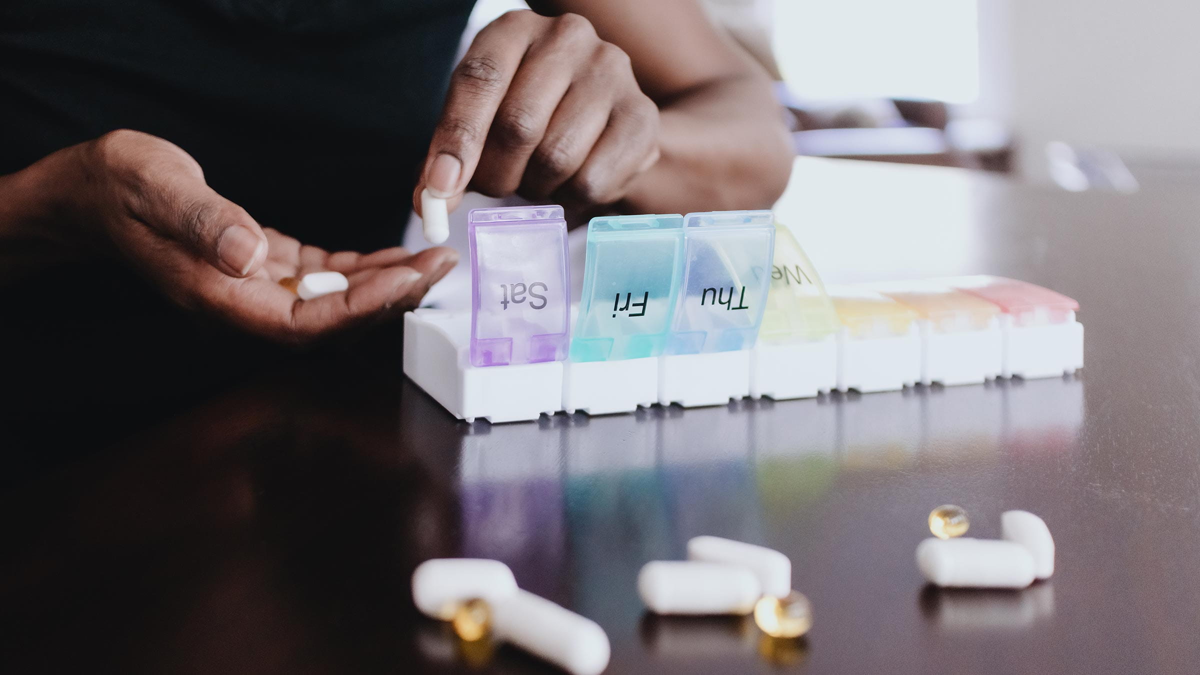 An African American woman organizes her vitamins and supplements into a pill box