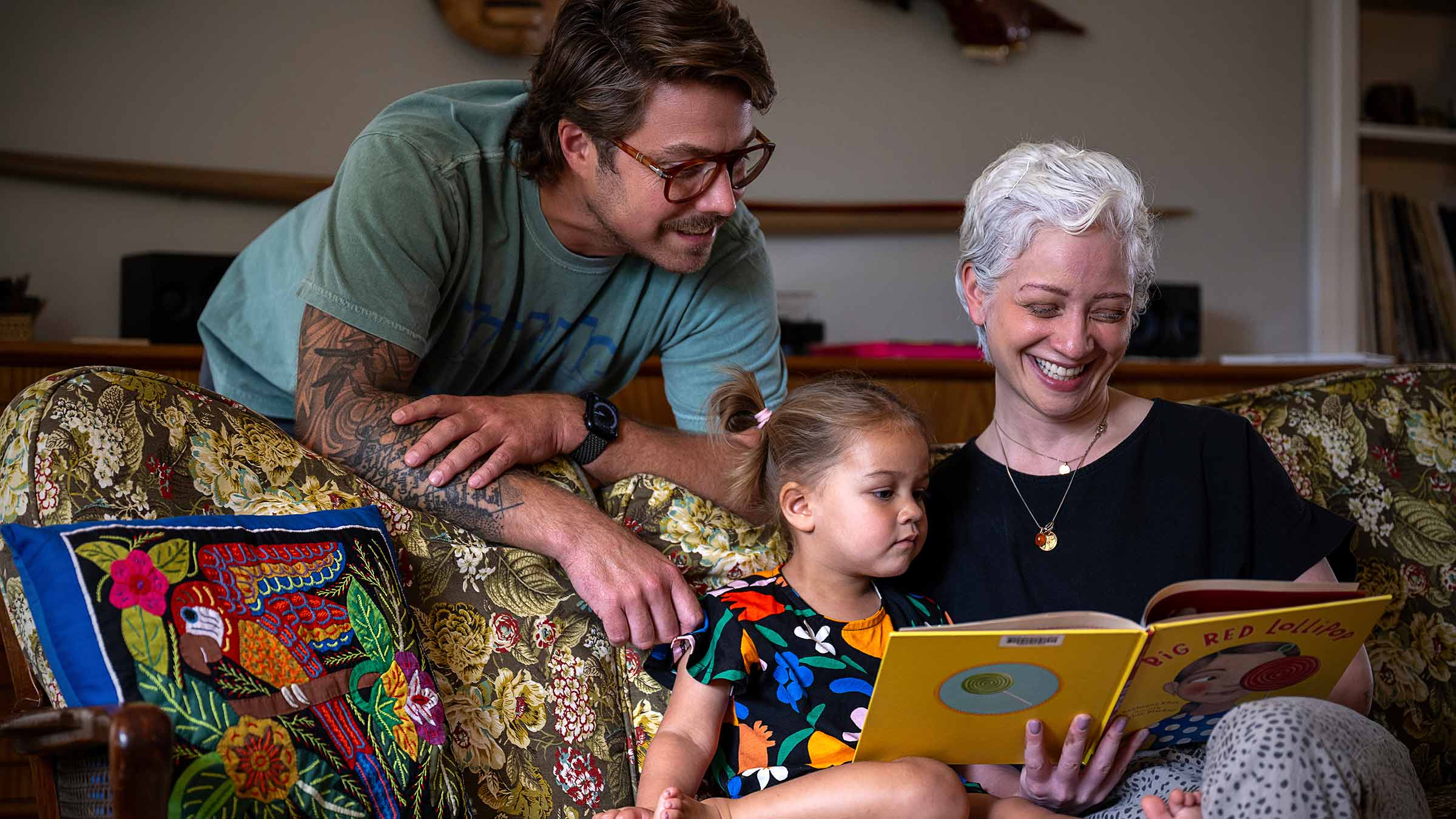 Sam de Silva at home reading a book with her husband and daughter