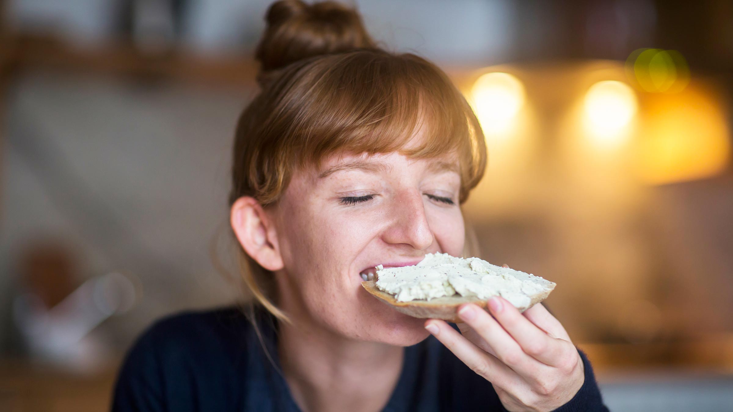 A young woman eating a piece of bread with cream cheese