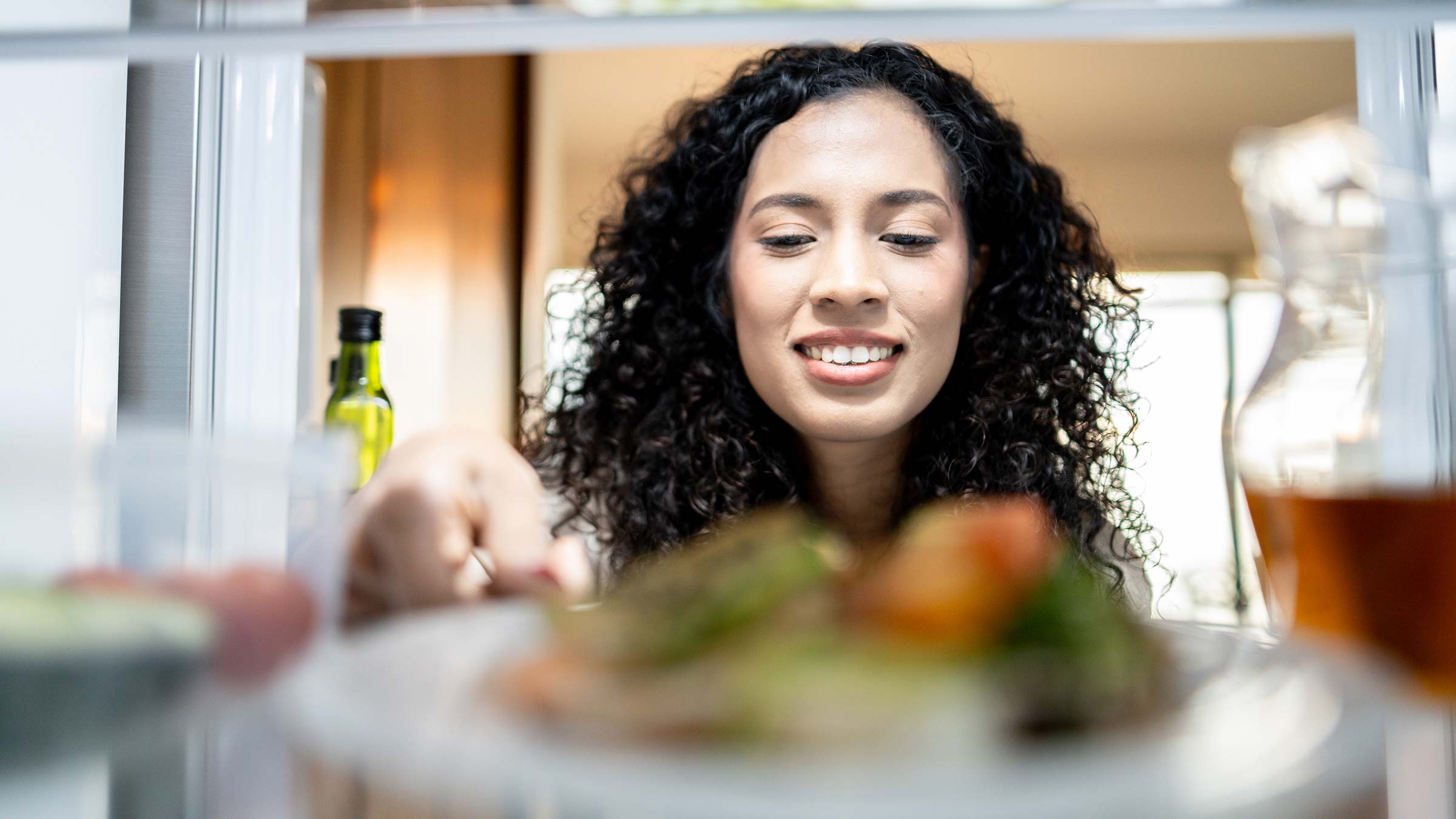 A woman reaching into her fridge to pull out food