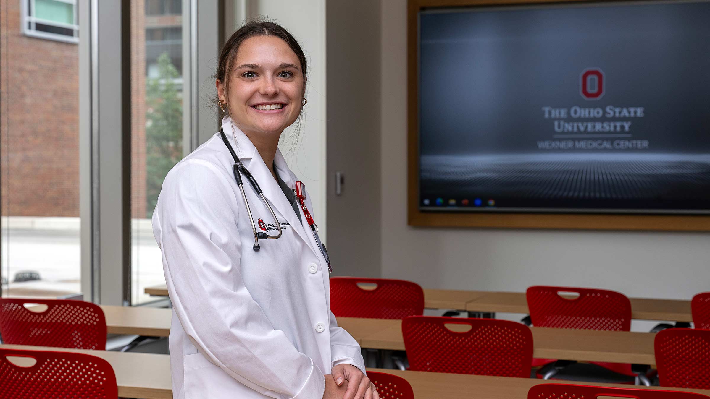Medical student, Hayley Zimbric, standing in a classroom in her medical uniform with a stethoscope around her neck