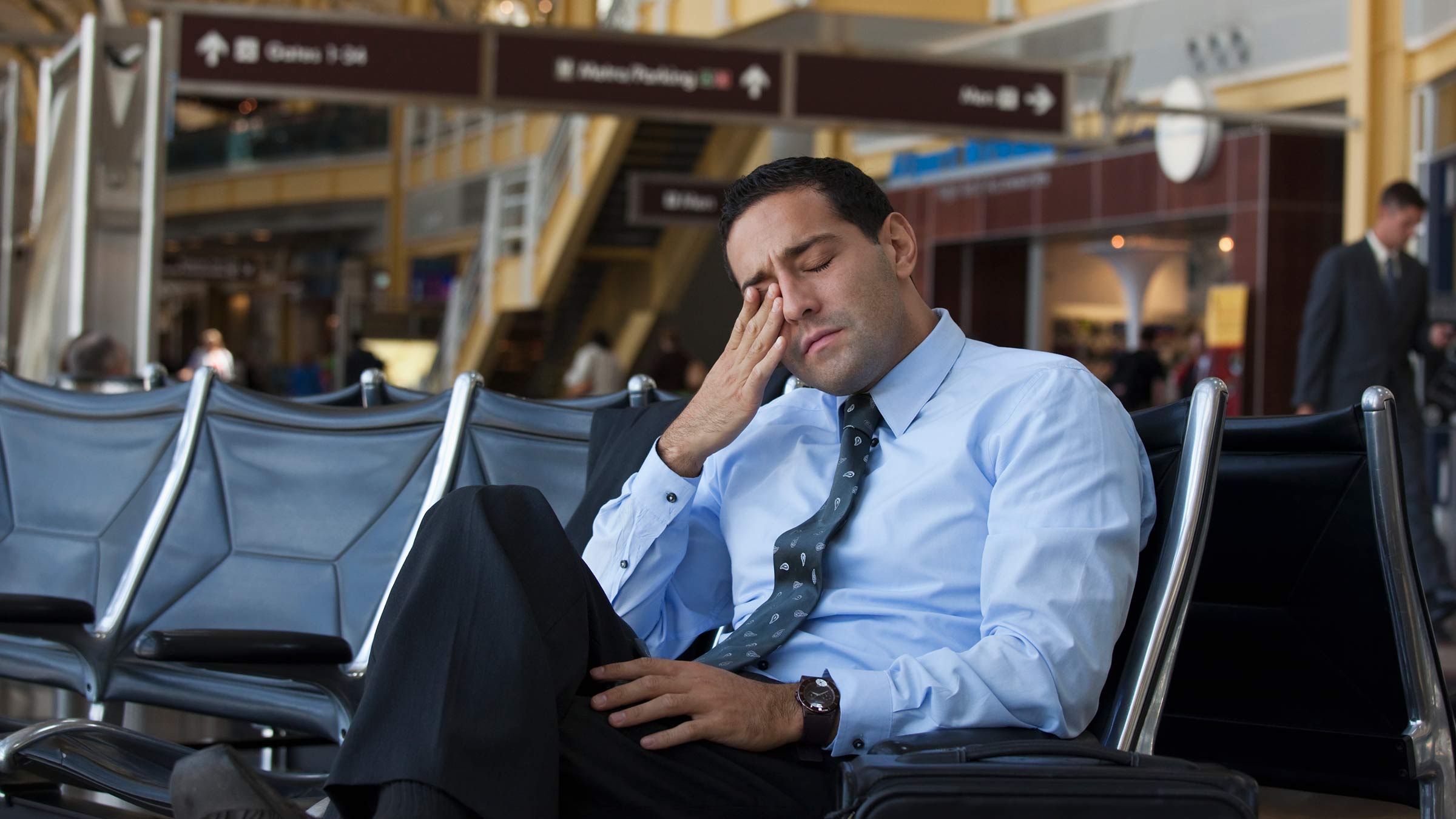 A tired young man rubbing his eyes in an airport