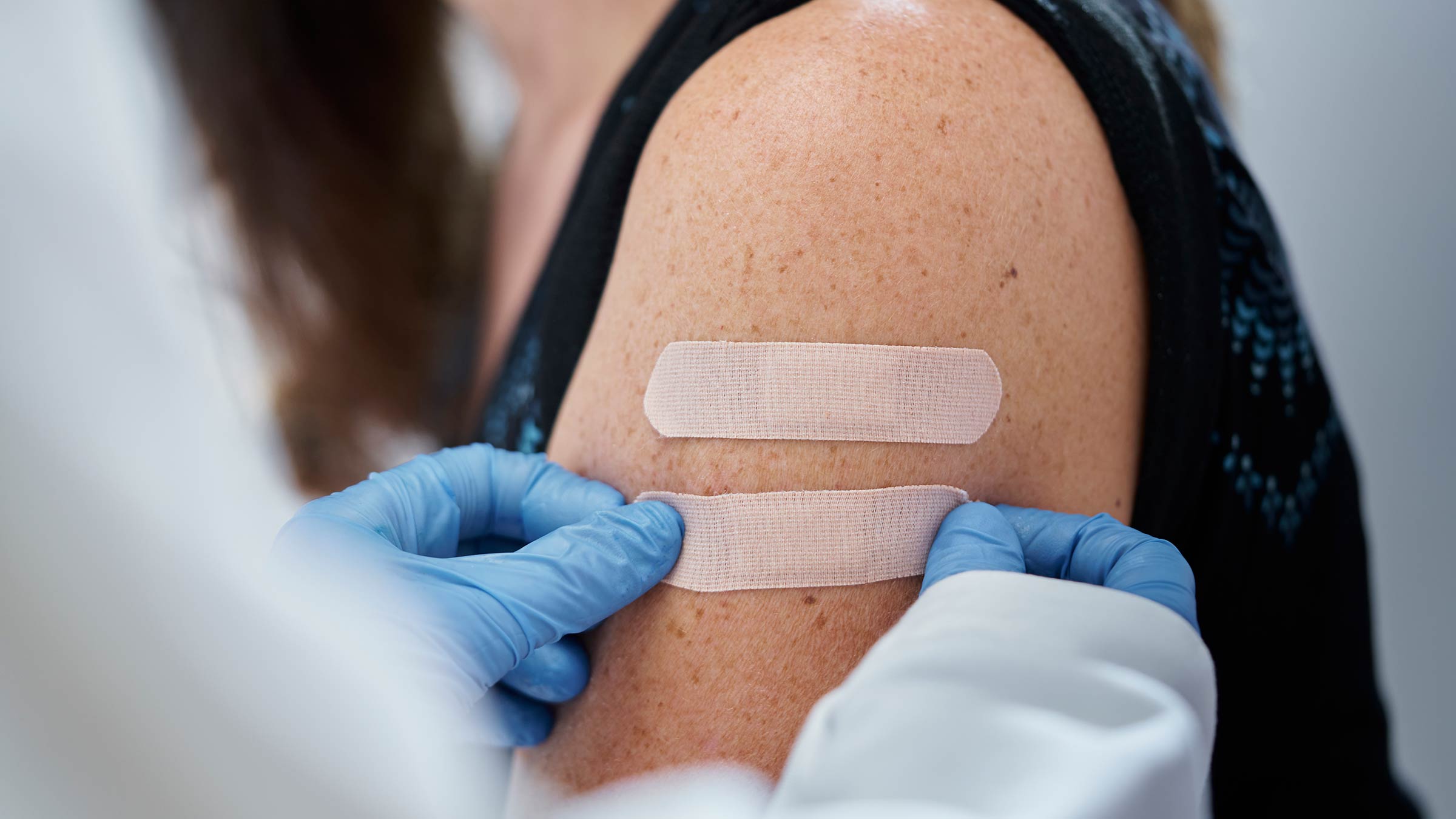 A doctor with gloves applying a second bandage to a woman’s arm after receiving a vaccine