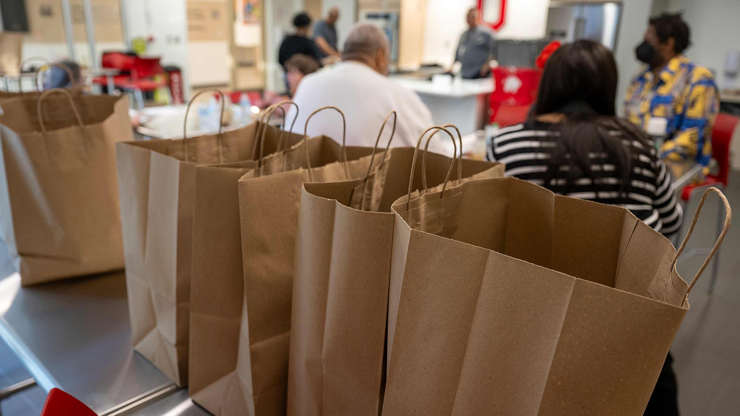 Paper bags lined up on the table with the people attending a cooking class on the background