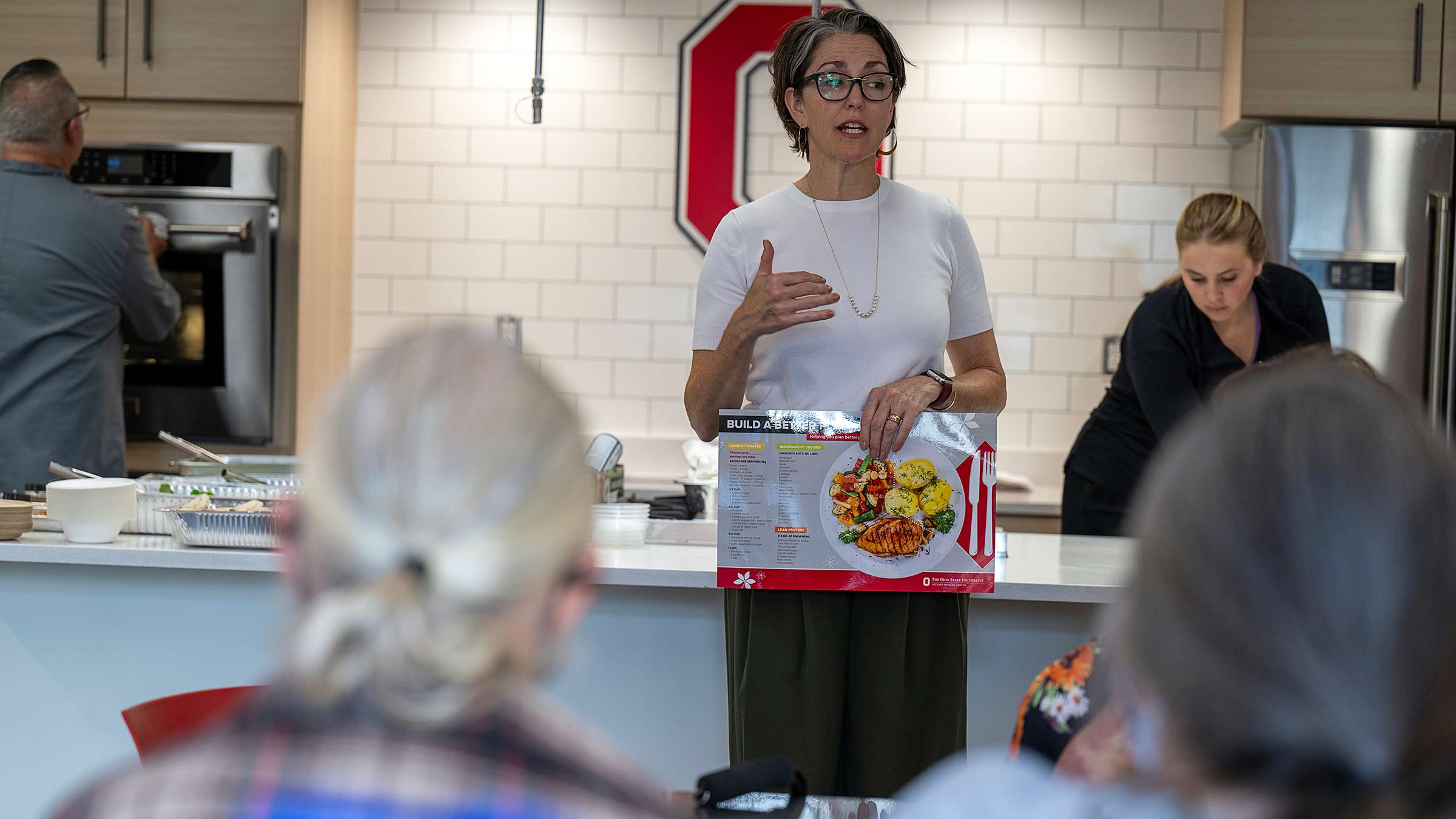 An educator holding a "Build a better plate" poster showing how much of each kind of foods should be on a plate