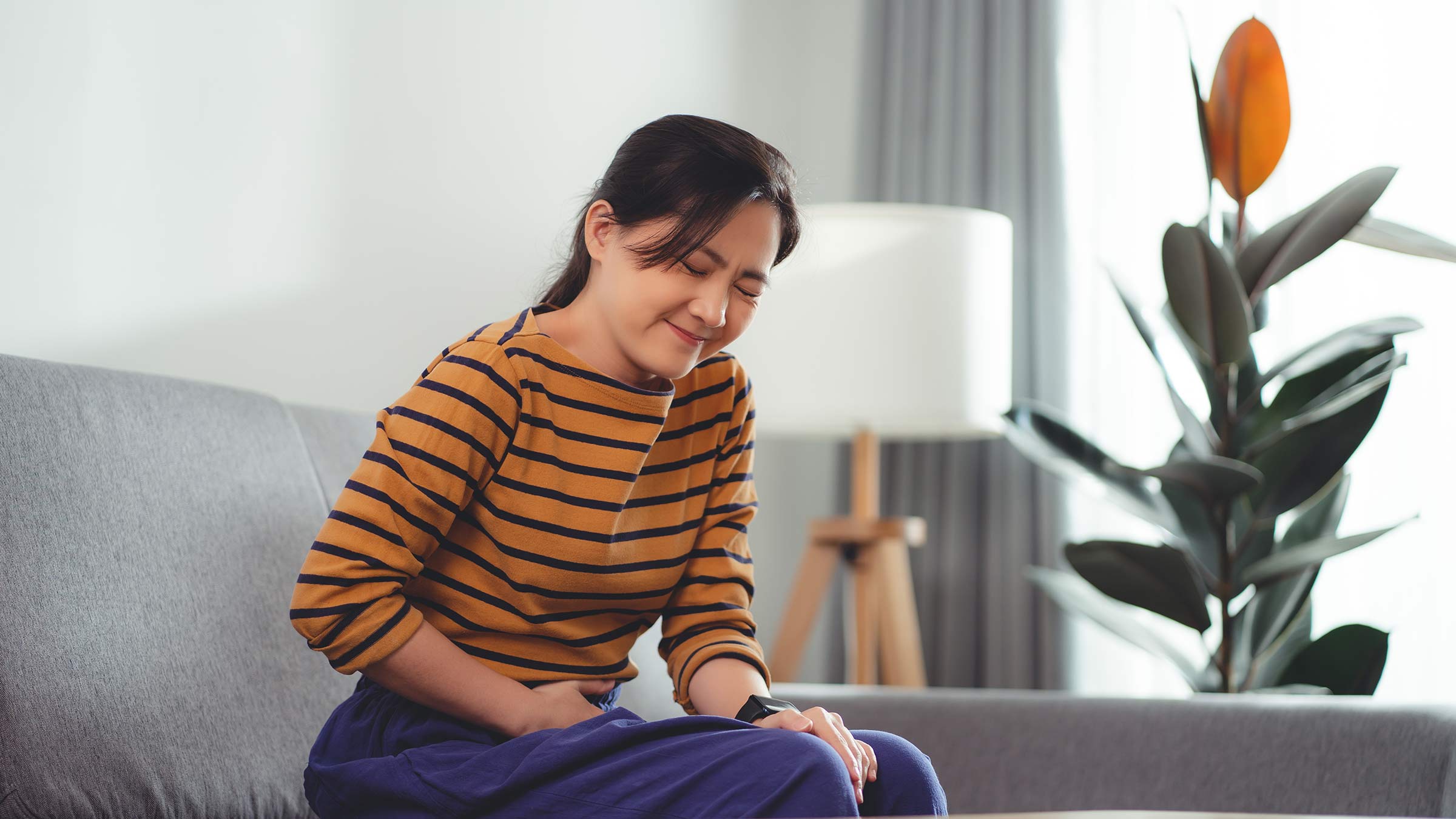 Woman sitting on a couch holding stomach and grimacing